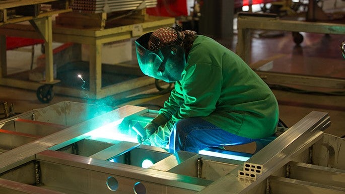 Welder lit up in green working on a trailer frame