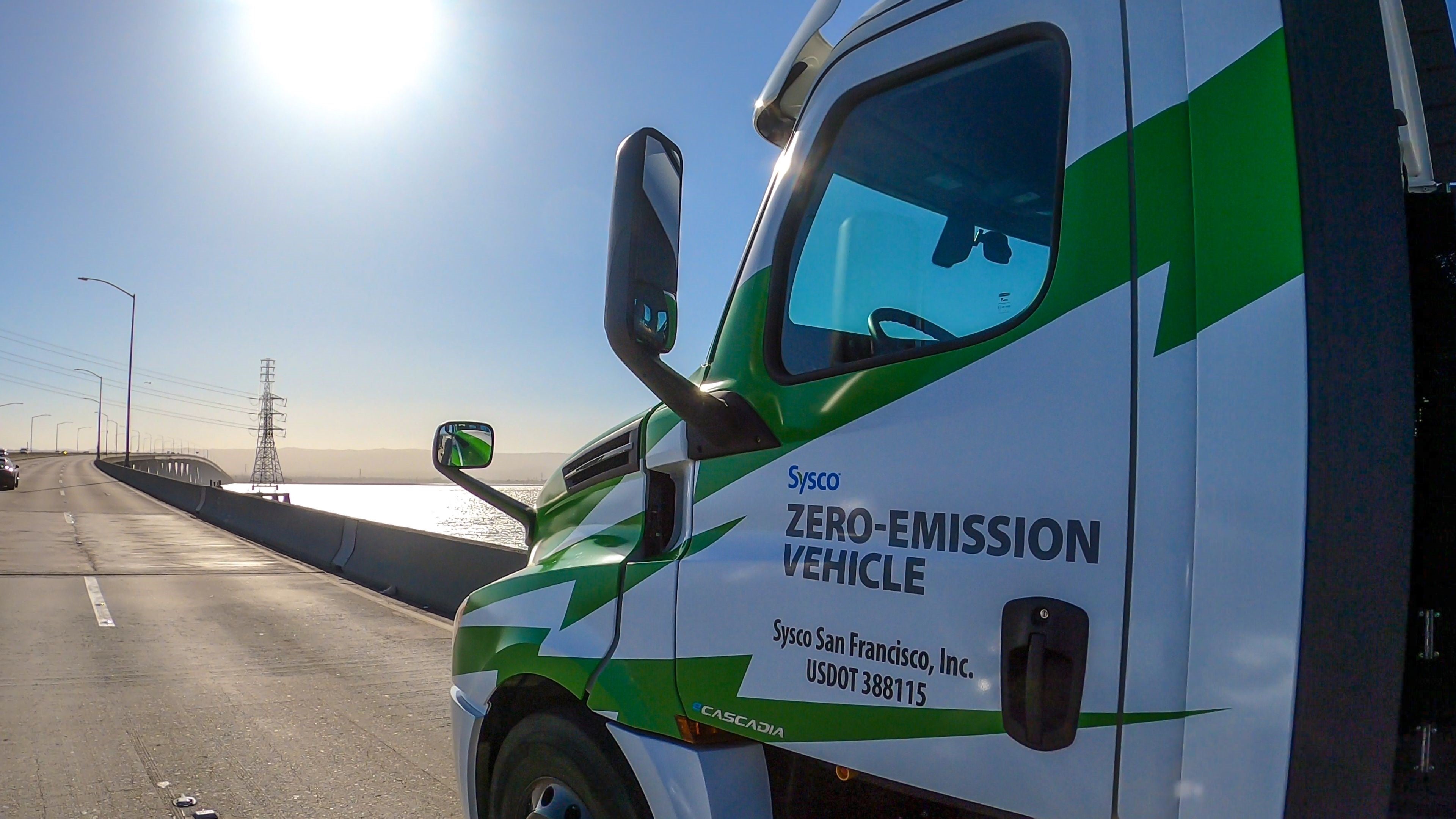 Driver's side view of white and green Freightliner eCascadia