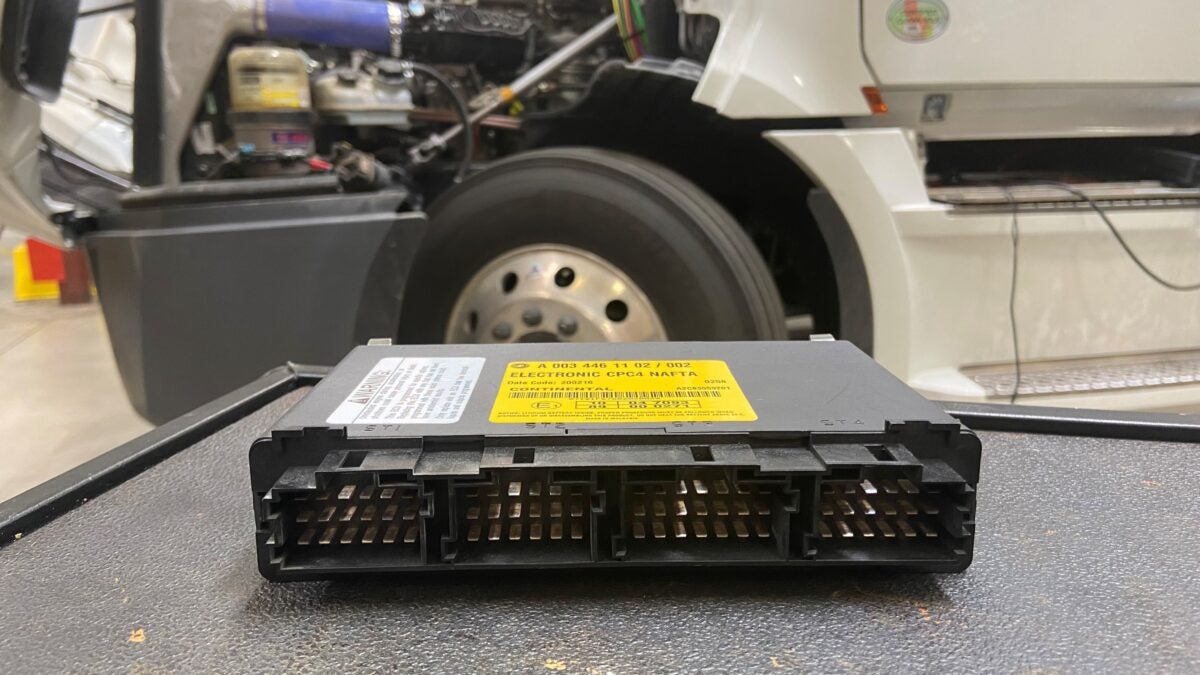 A black and yellow powertrain module in the foreground with a Freightliner truck behind it.