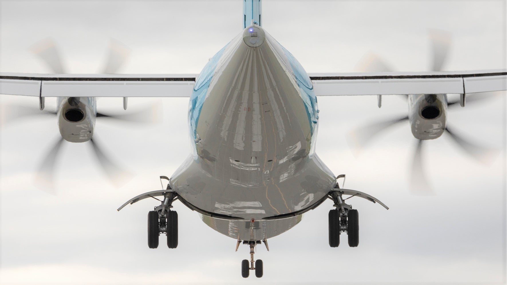 A propeller plane viewed from behind with wheels out and still in the air above runway.