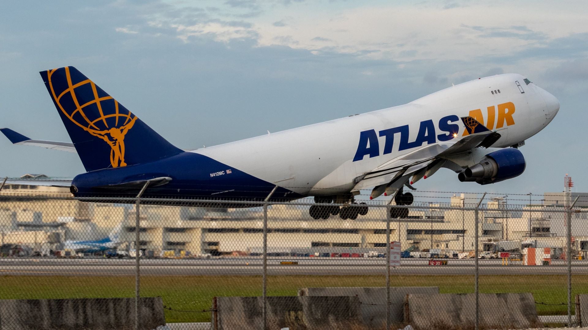 A big cargo jet, white with a blue tail and Atlas Air painted on the side, lifts of the runway in this sideview.