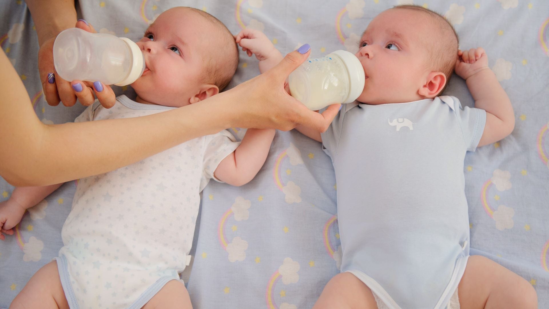 Twin babies on their back being fed from bottles.