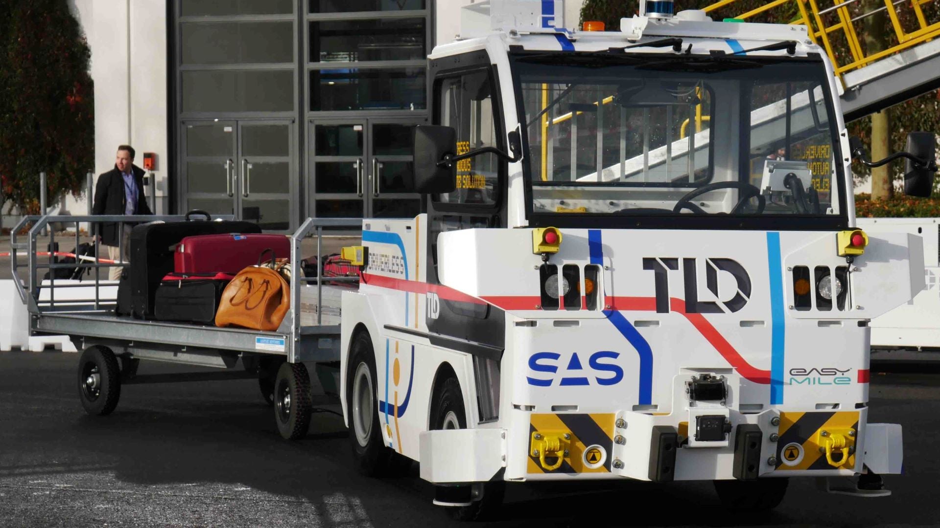 A white industrial yard tractor that moves without a driver.