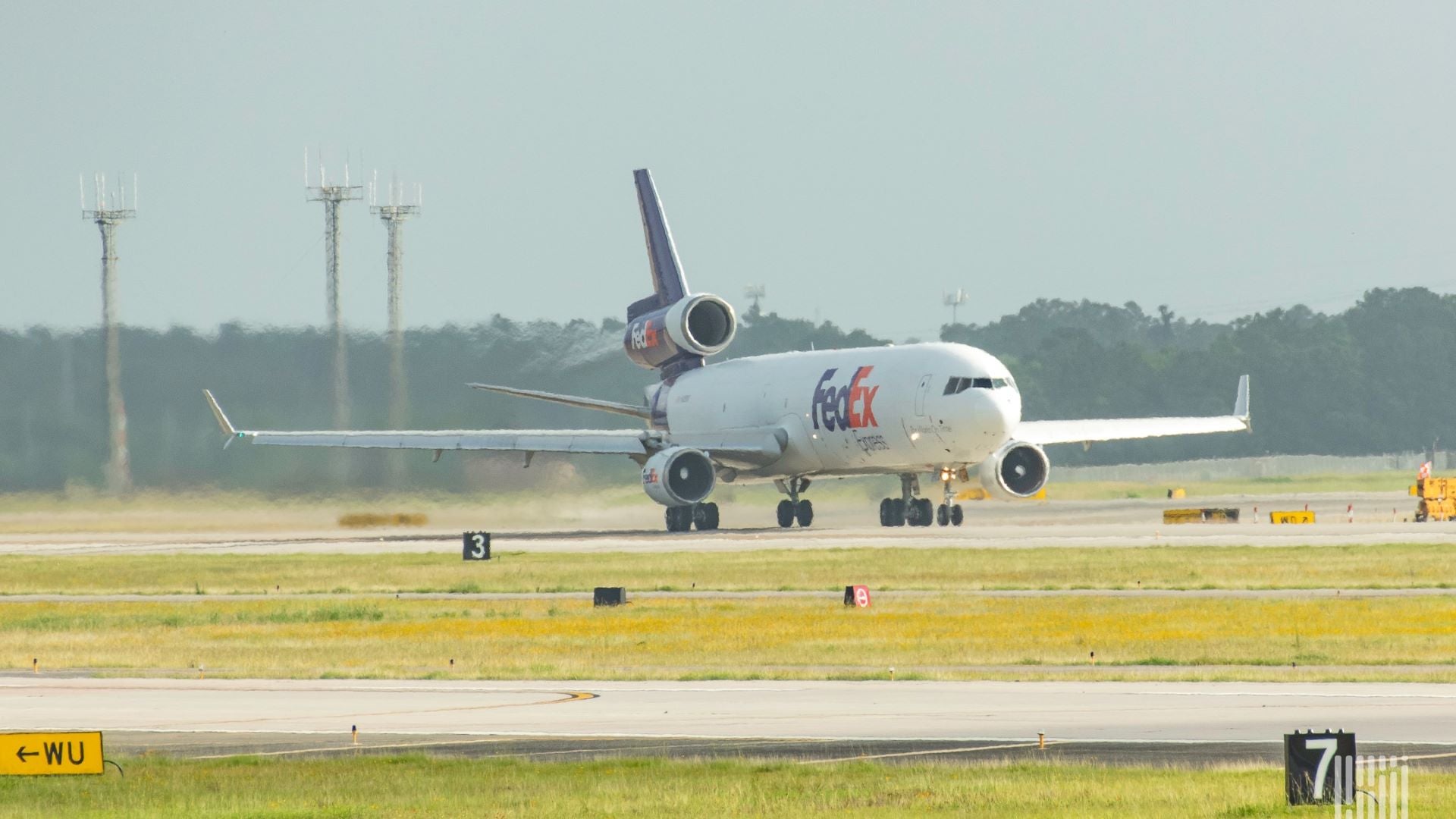 A large, white FedEx plane with blue tail rolls down the runway, heading toward camera.