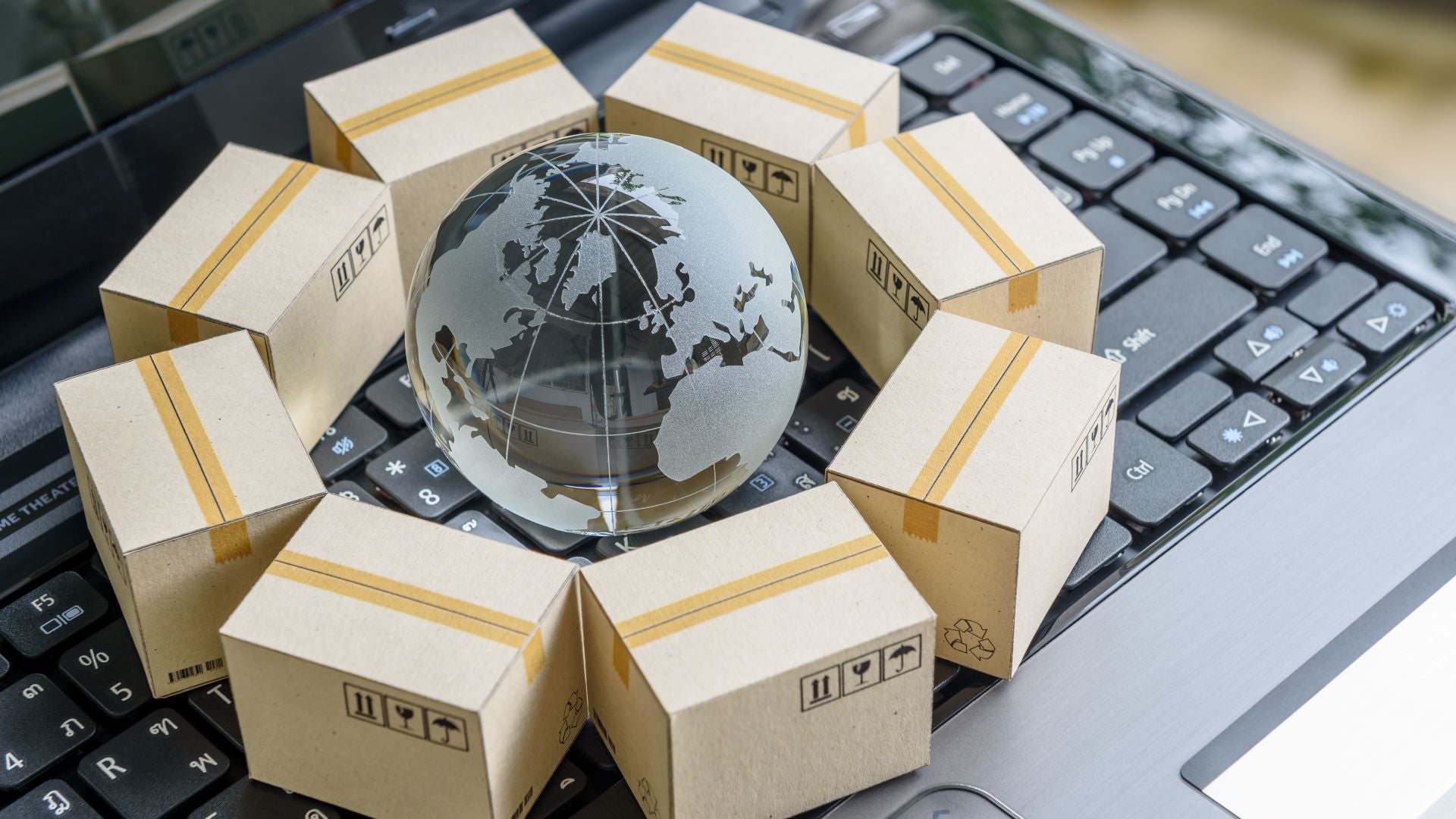 Shipping boxes and a glass globe on a keyboard signifying digital trade.