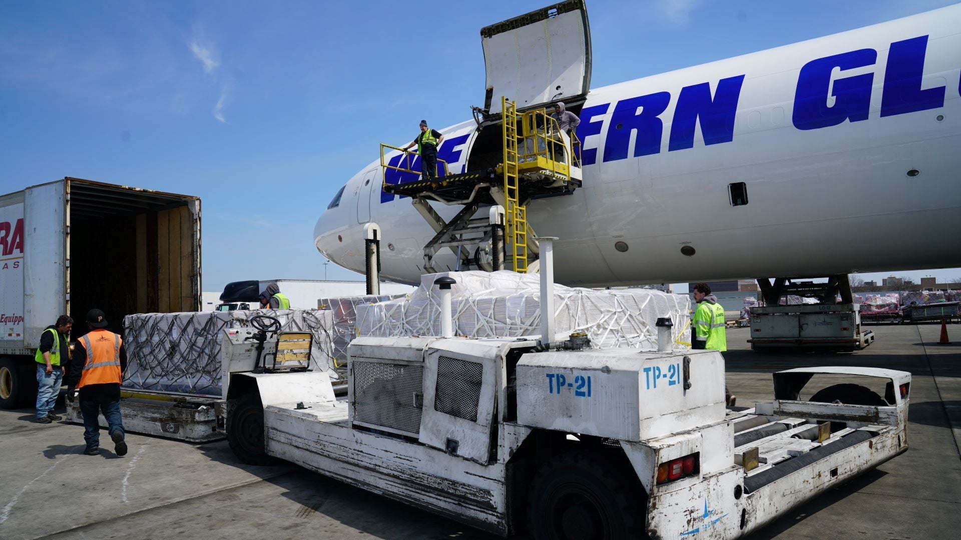 Cargo on a pallet waiting to be loaded onto a plane labeled Western Global, cargo door open on sunny day.