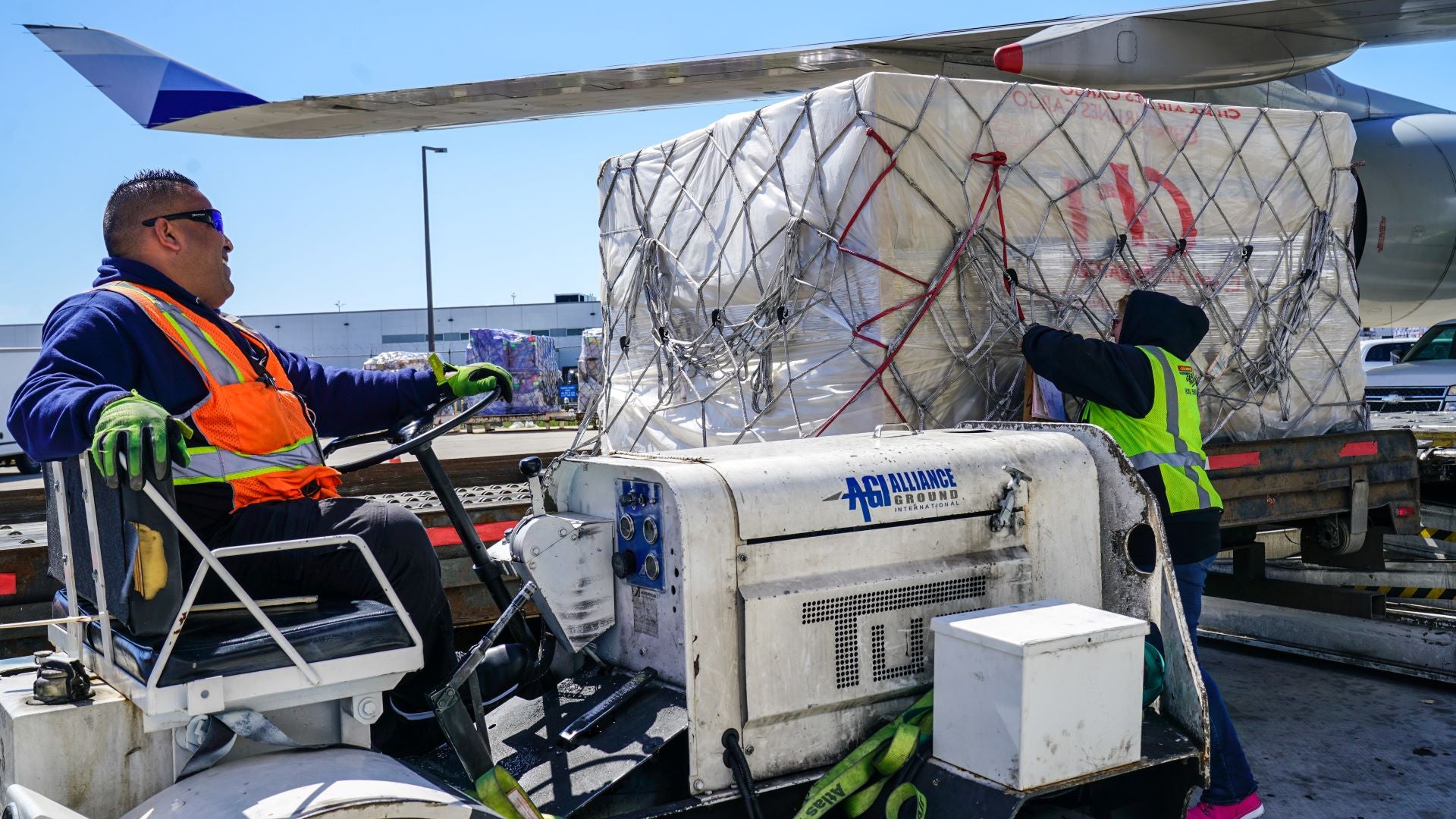 Ground personnel use a tug to position a cargo pallet next to a plane.