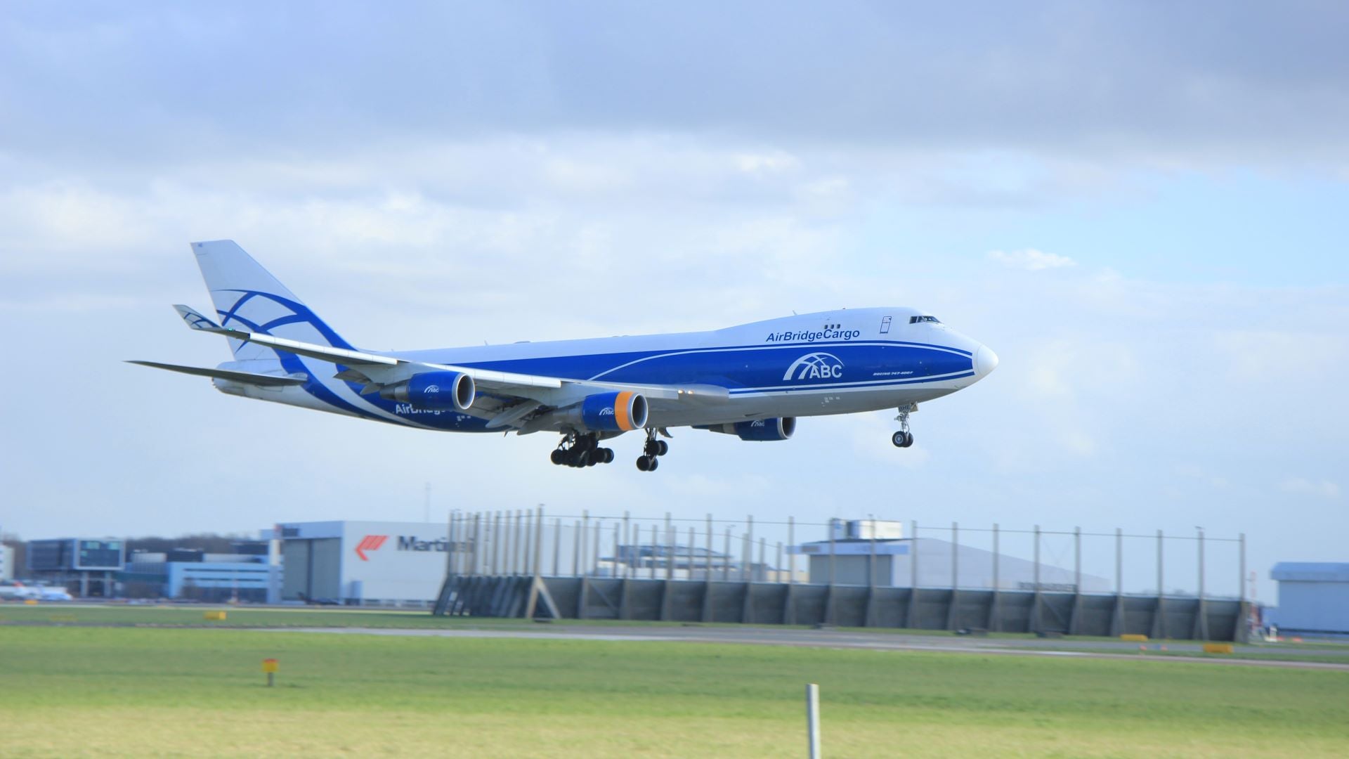 A white-and-blue jumbo jet with AirBridgeCargo logo about to land on runway.