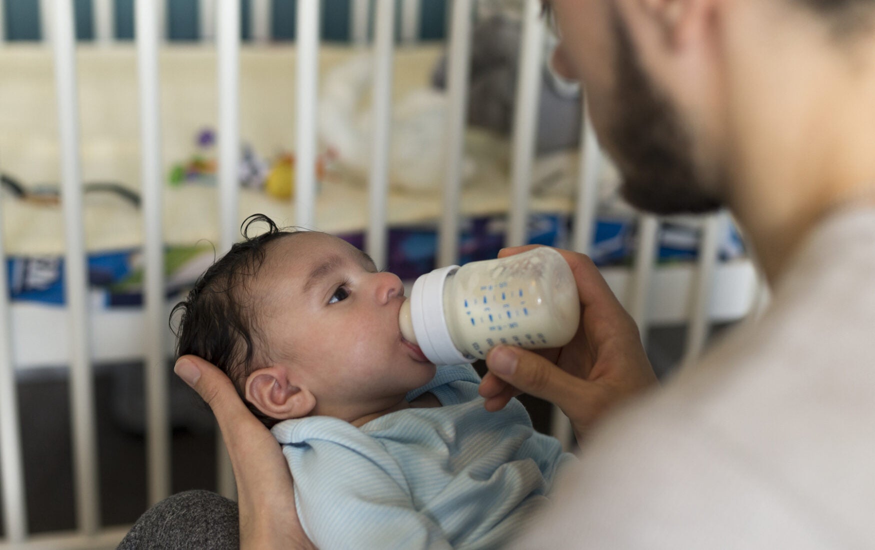 A baby is fed formula from a bottle being held by a man in a beard.