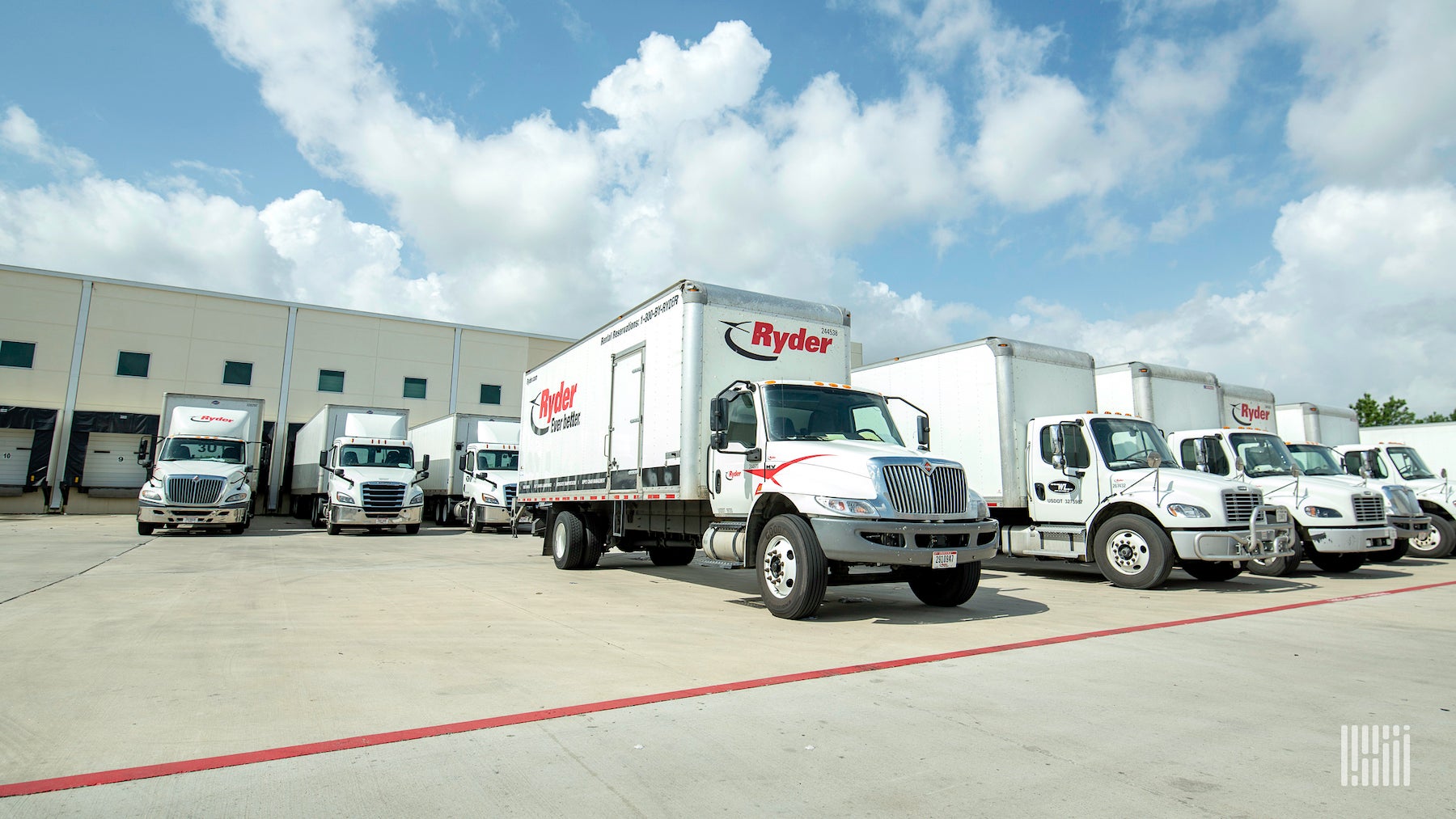 Nine trucks with the logo of Ryder written on them are parked at a facility