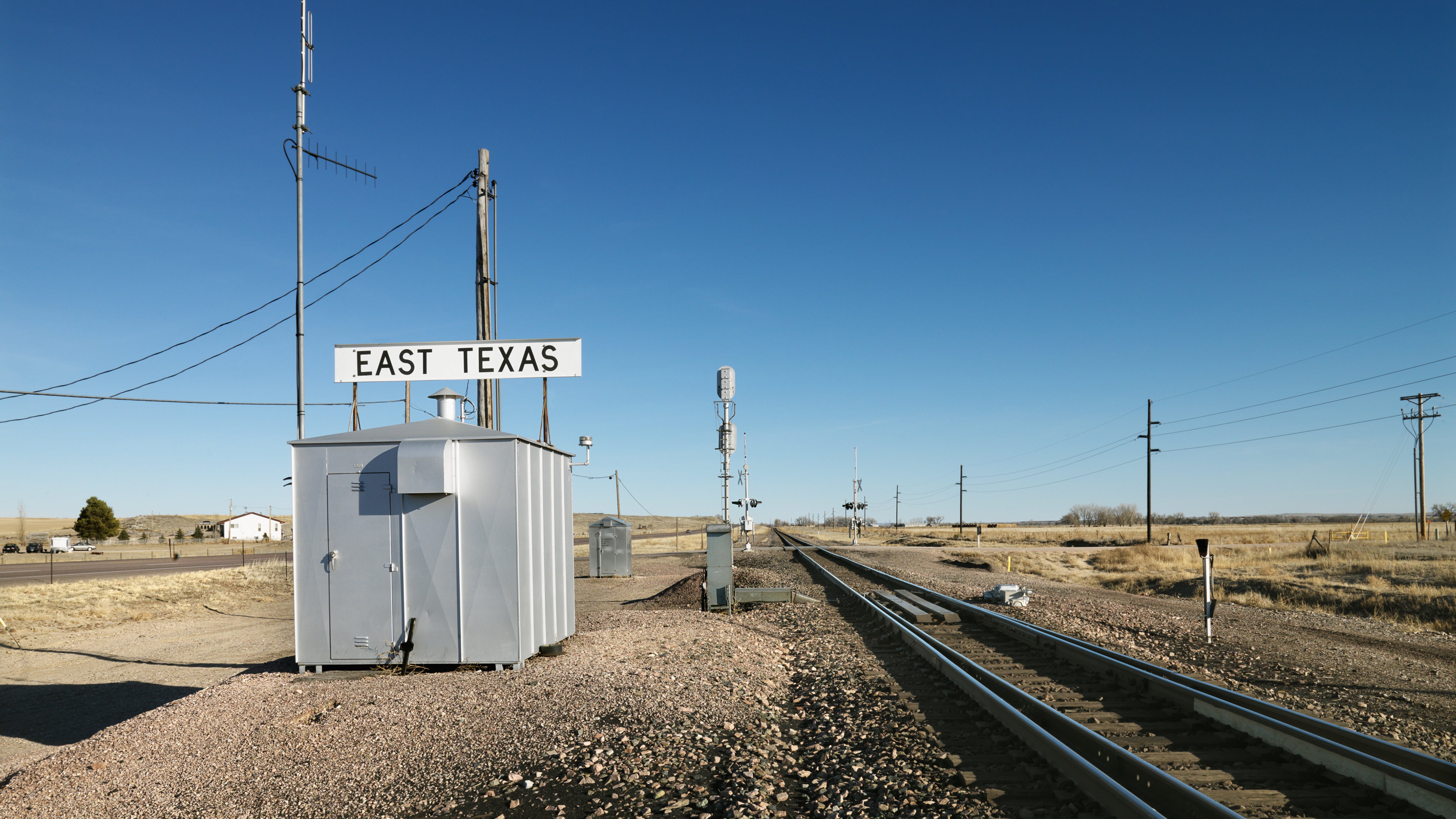 A photoraph of a rail track in a desert-like field. A small building with a sign that says East Texas is next to the track.