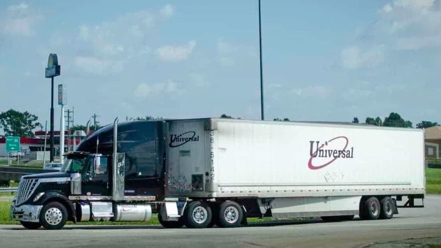 A black tractor pulling a white Universal trailer