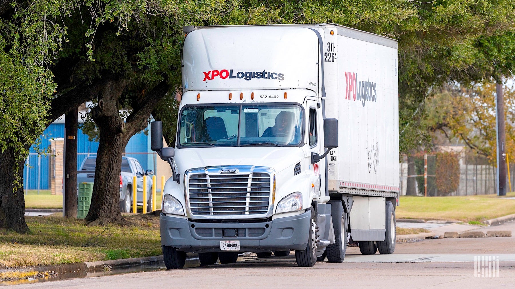 A white tractor-trailer with the red and black logo of XPO Logistics visible on the front and side, parked on a street