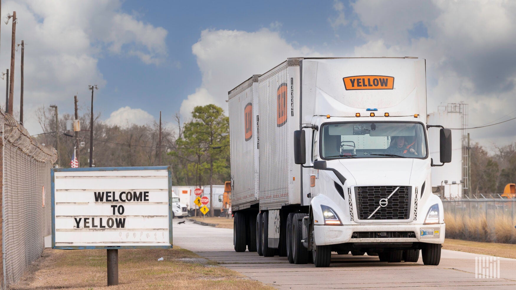 A semi truck with a double trailer with the logo of the company Yellow driving on a road next to a sign reading Welcome to Yellow