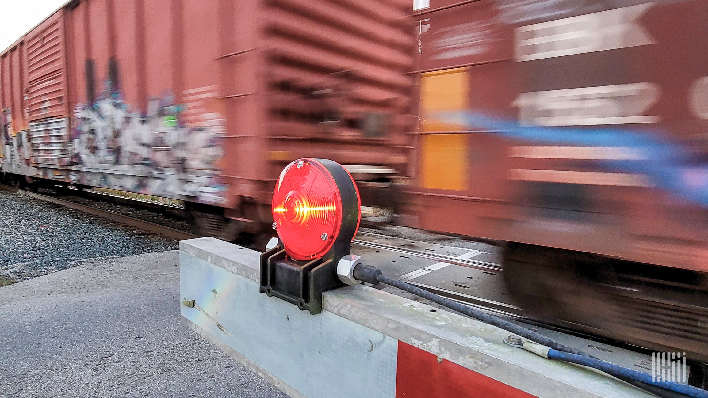 Boxcars whizzing by a blocked rail crossing.