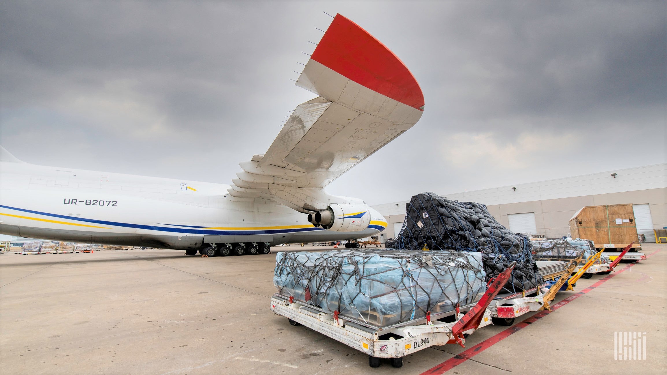 A large pallet of cargo sits on tarmac near a big cargo aircraft.