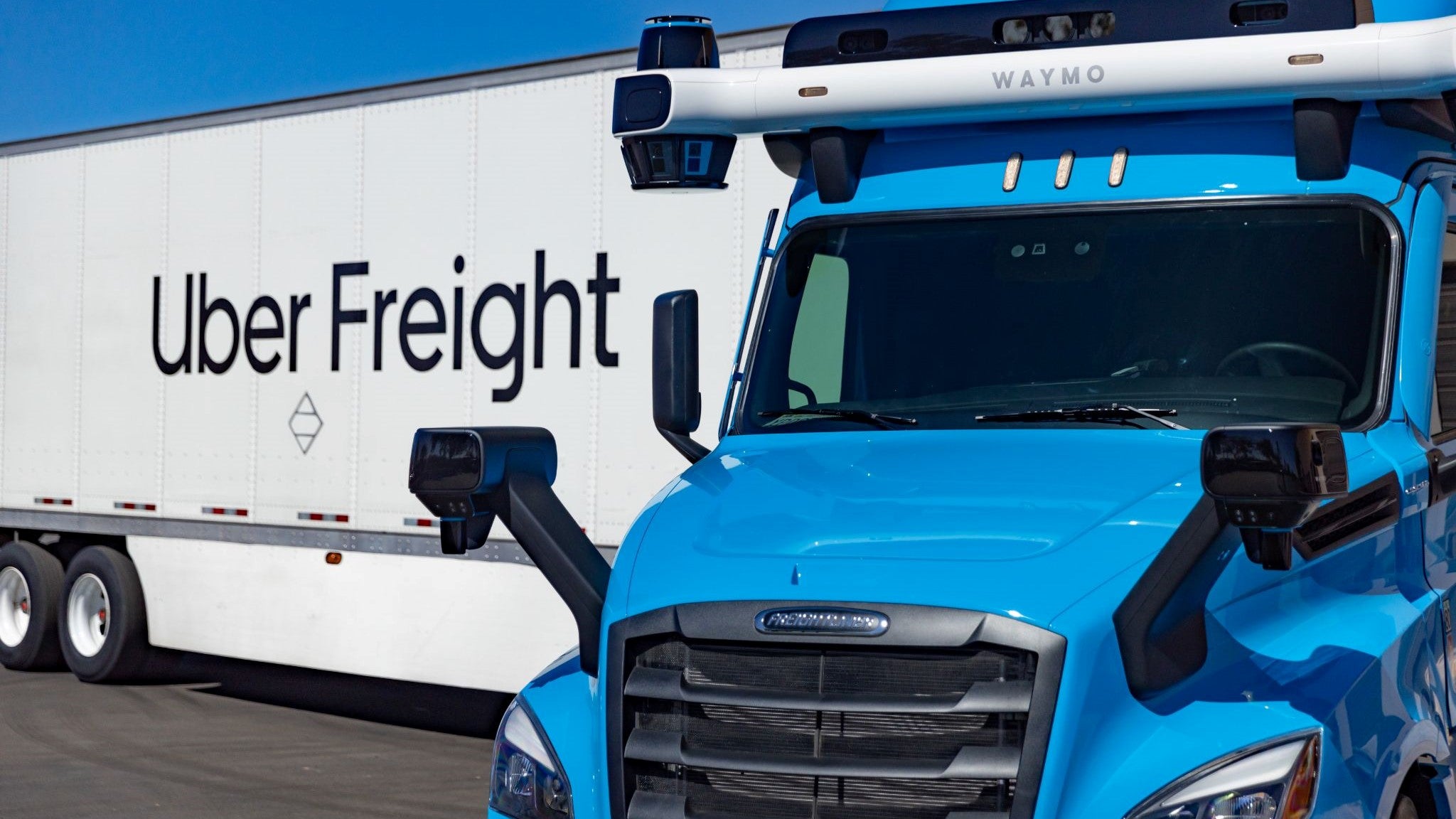 Waymo Via truck in blue connected to white Uber Freight trailer