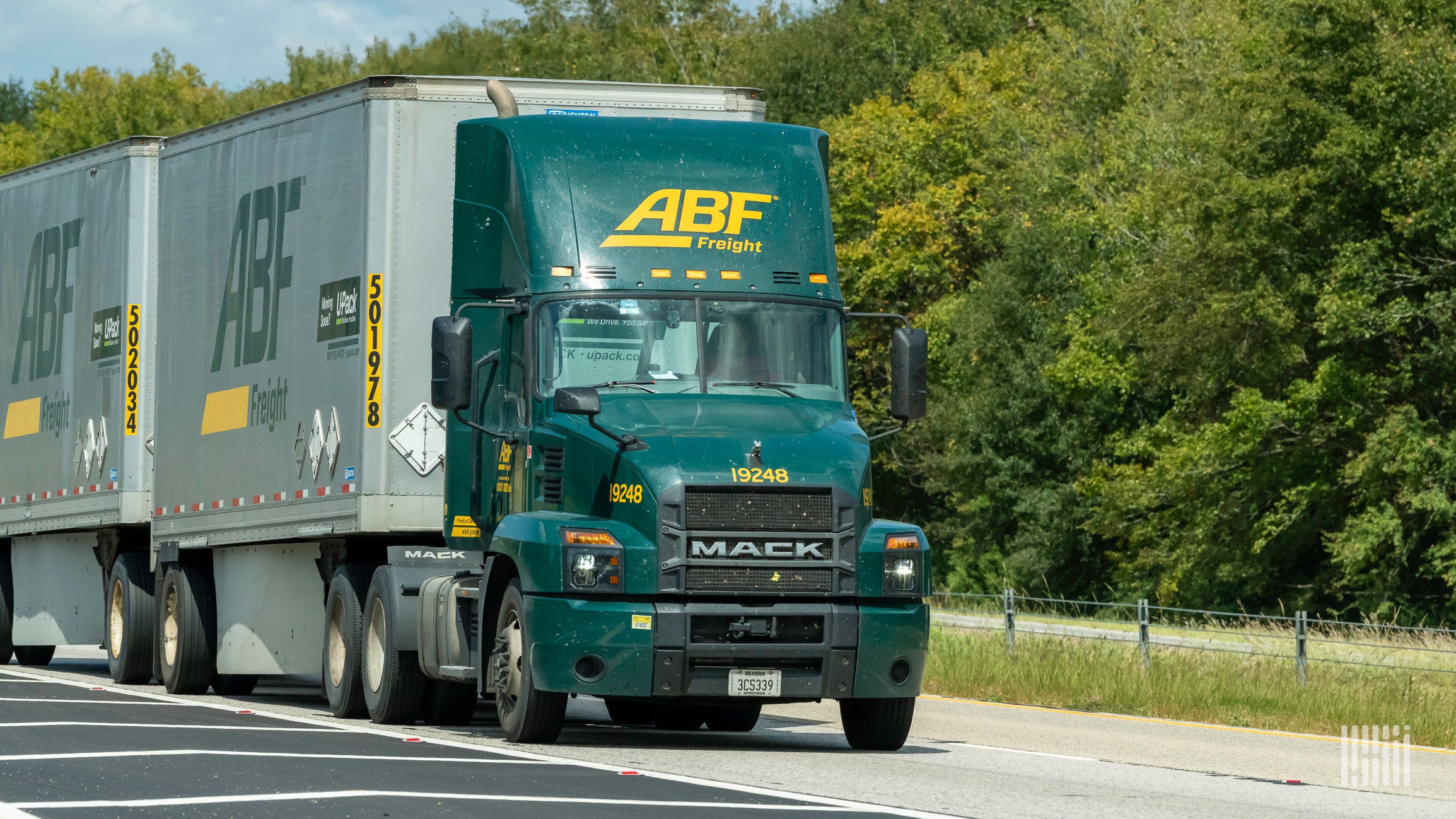 A green ArcBest tractor pulls a silver trailer on a road in front of green trees.