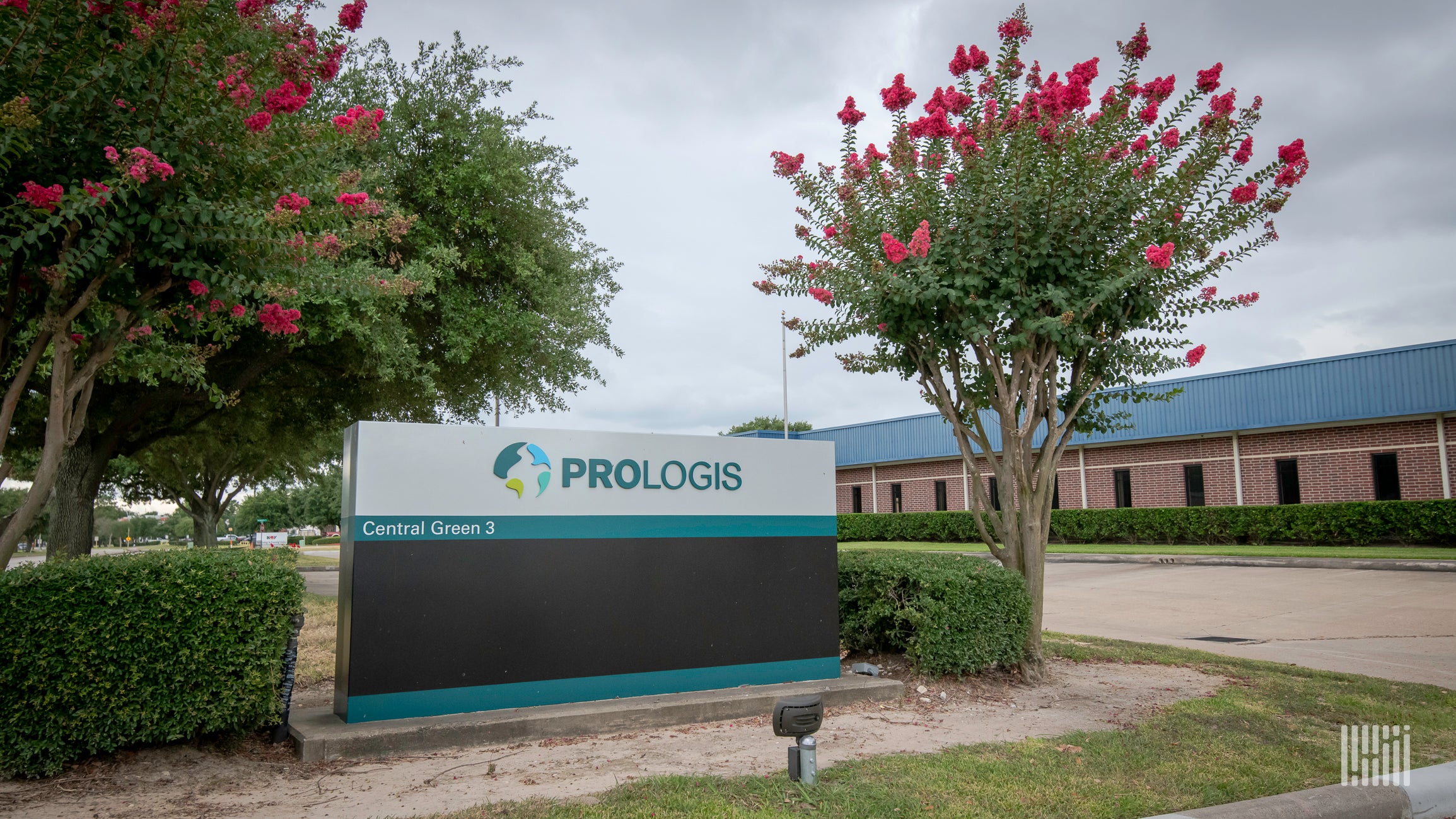 Green trees surround a Prologis sign in front of a warehouse.