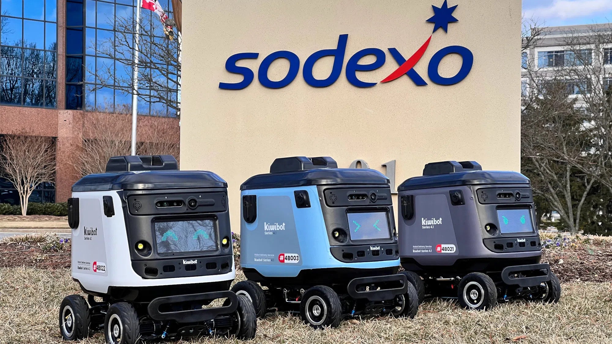 3 delivery robots parked on lawn in front of Sodexho sign