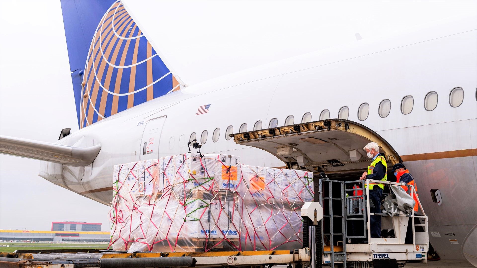 A pallet on a lift being loaded into rear of white United jet with blue tail .