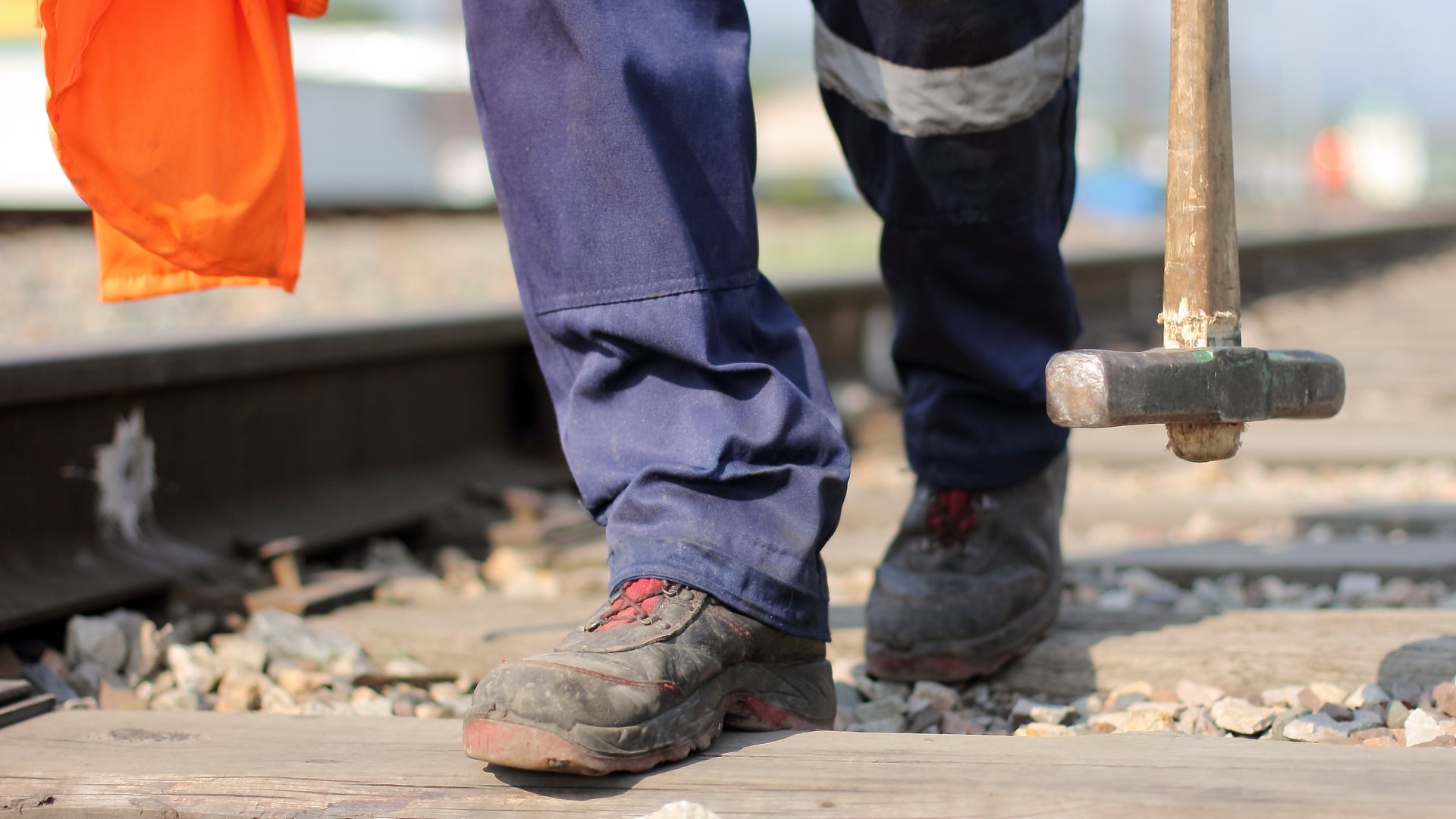 A man walks along a railroad track holding a sledgehammer