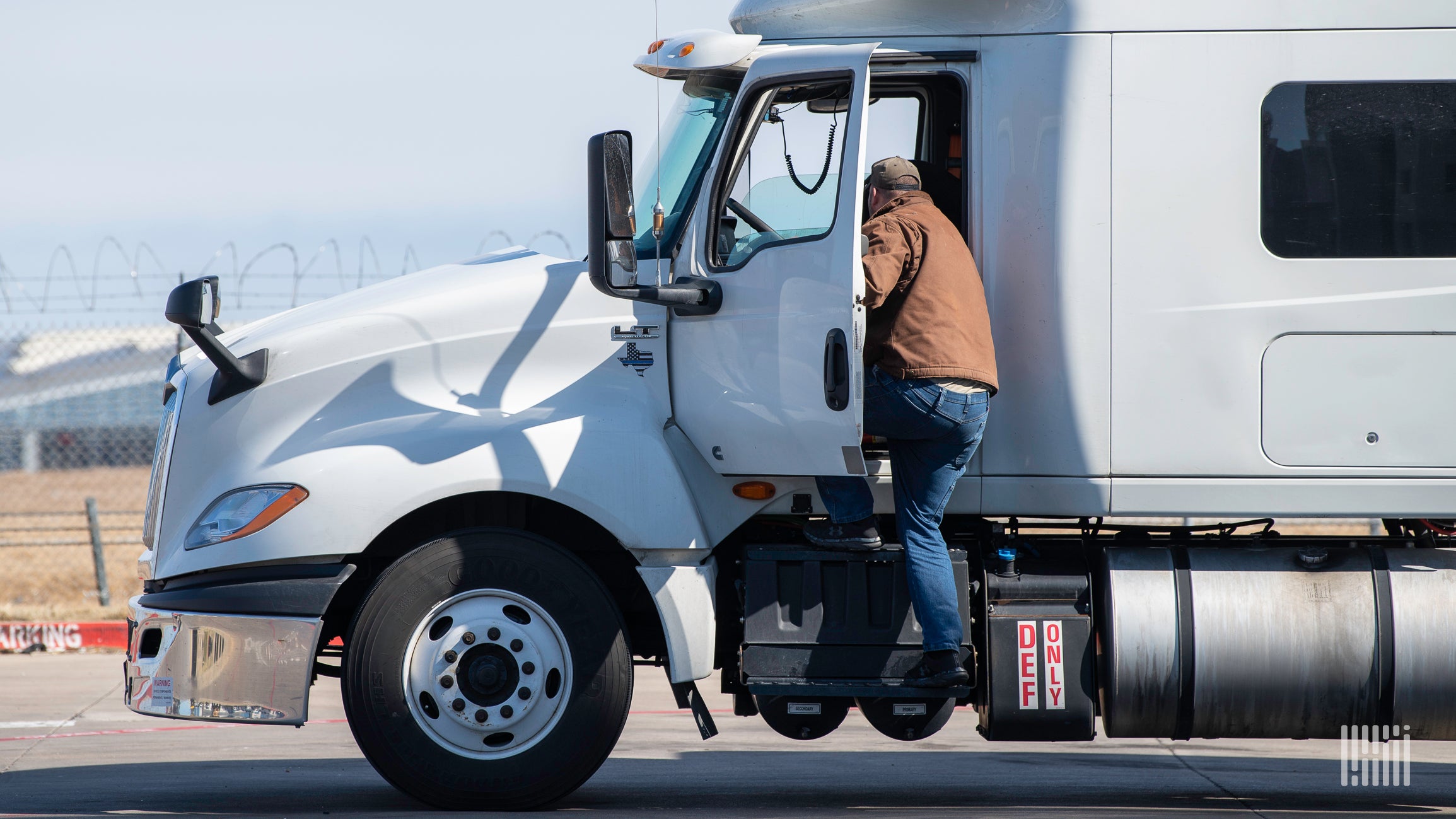 A driver steps up into the cab of a Class 8 tractor.