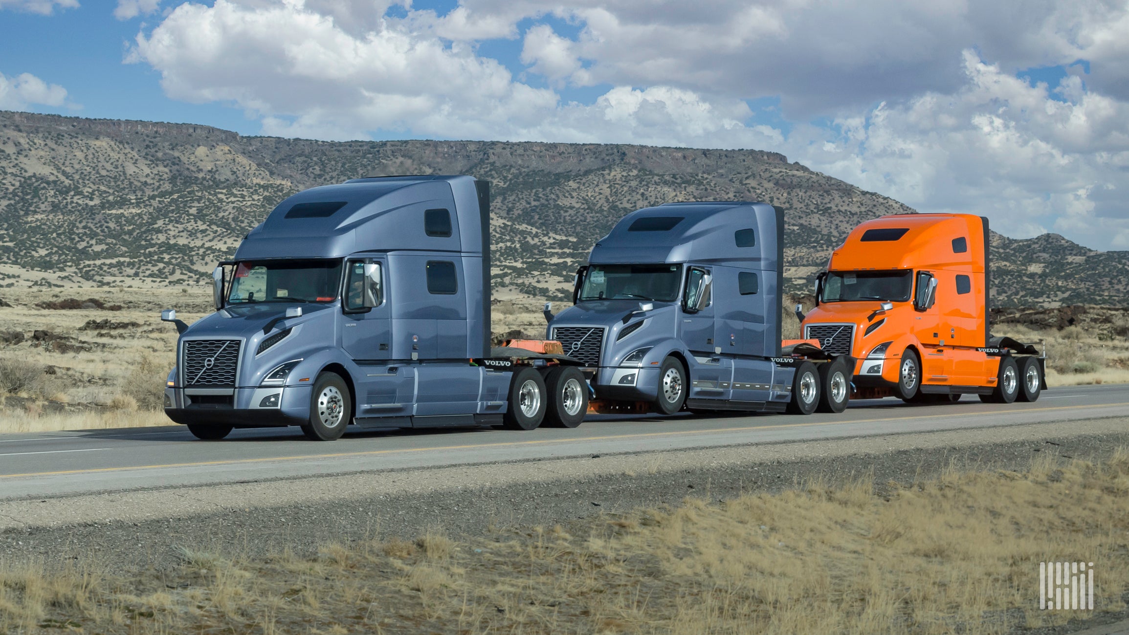 Two blue and one orange Volvo sleeper cabs on a highway