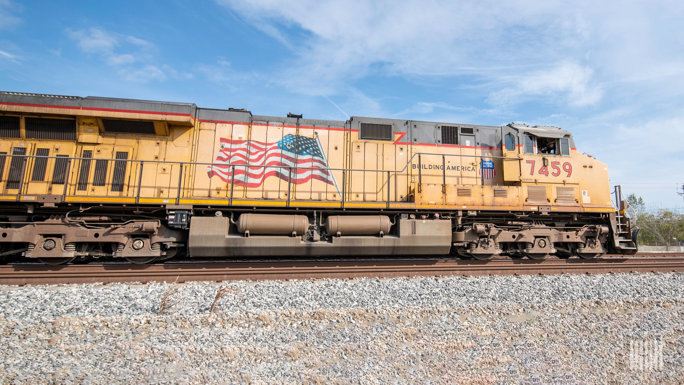 A yellow Union Pacific locomotive travels along train tracks with a blue sky in the background.