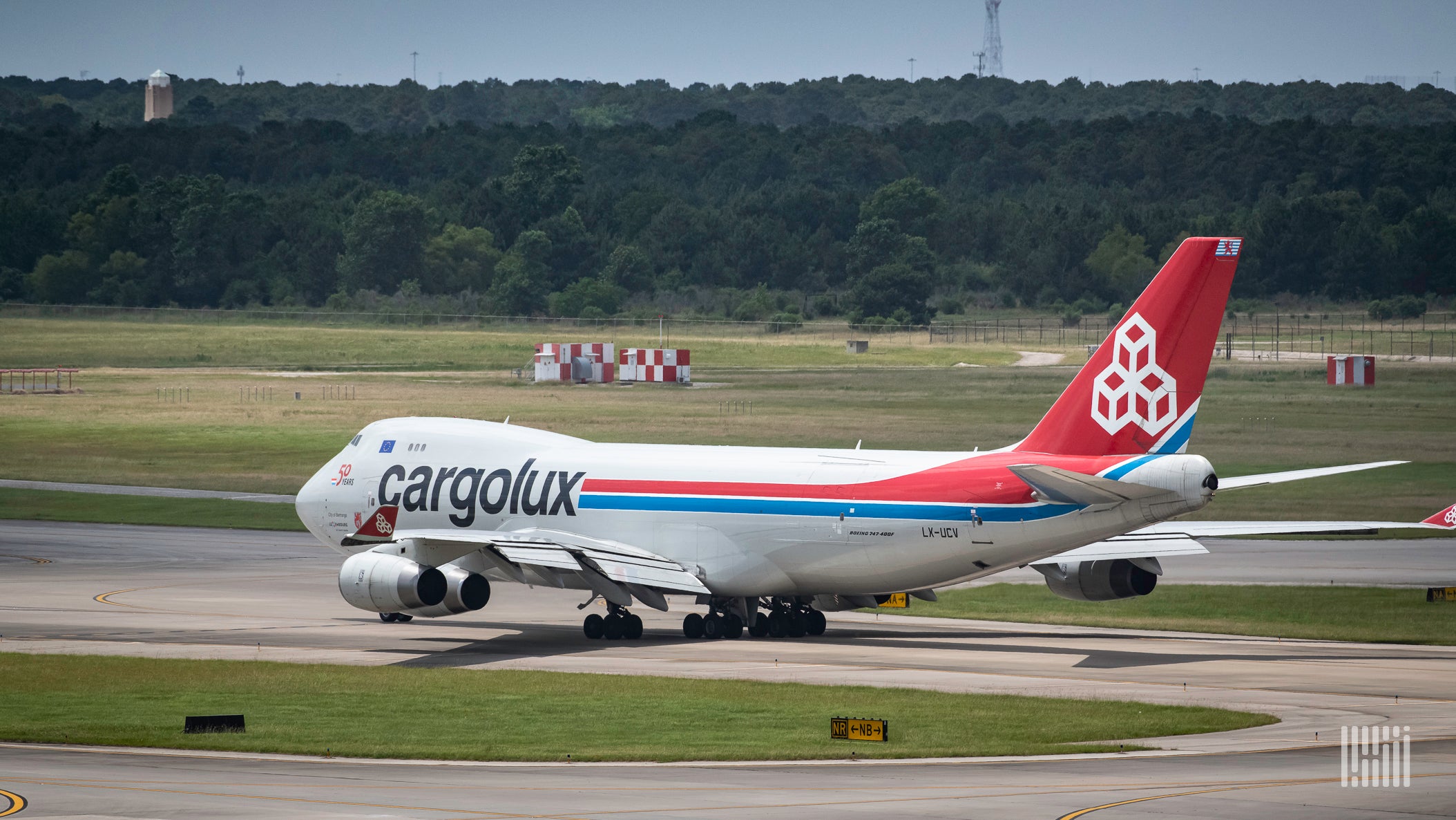 A white Cargolux jumbo jet with red tail prepares to take off. View from the rear.