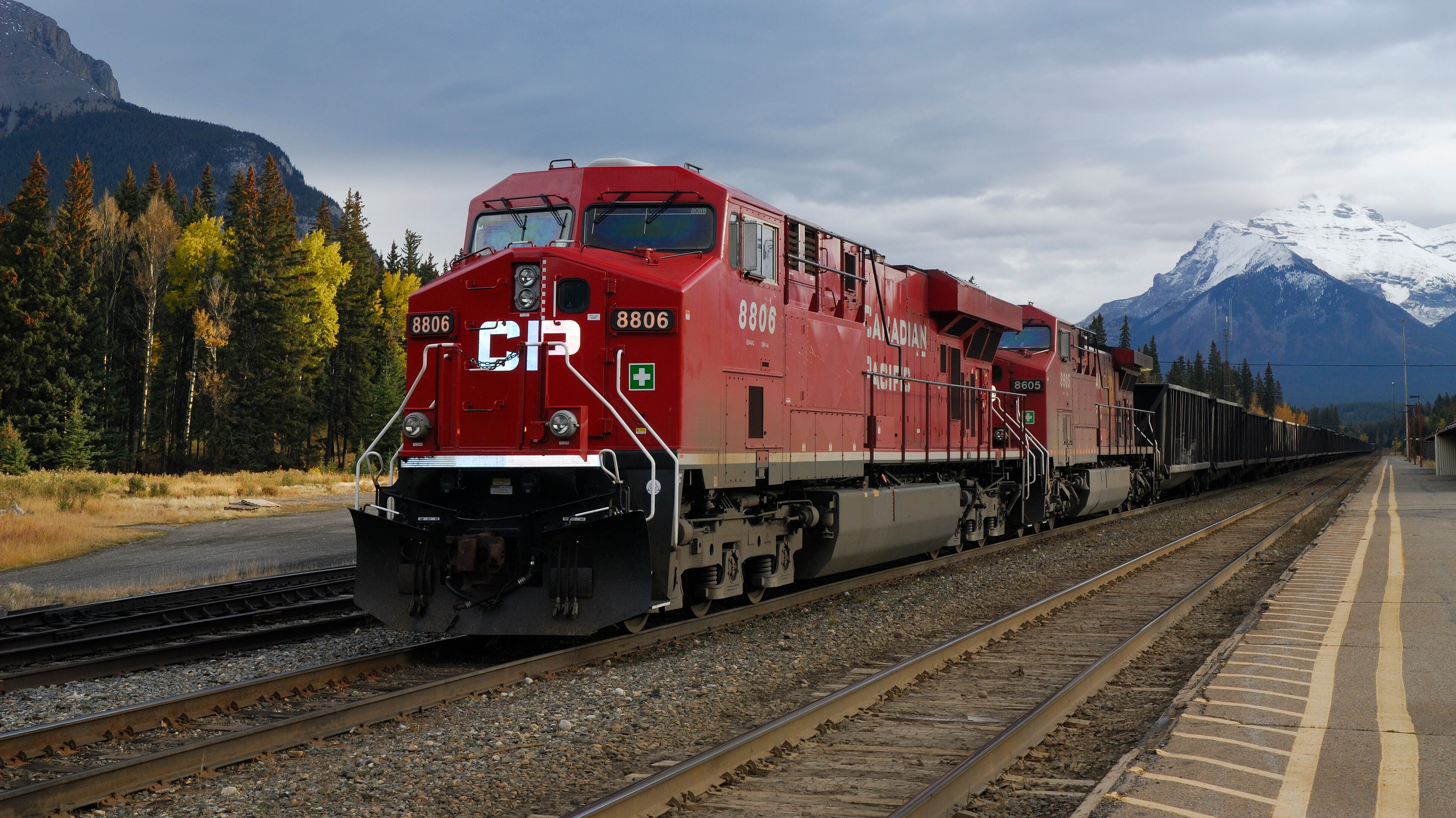 A train with the letters "CP" painted on the front of a locomotive travels in front a snow-capped mountain.