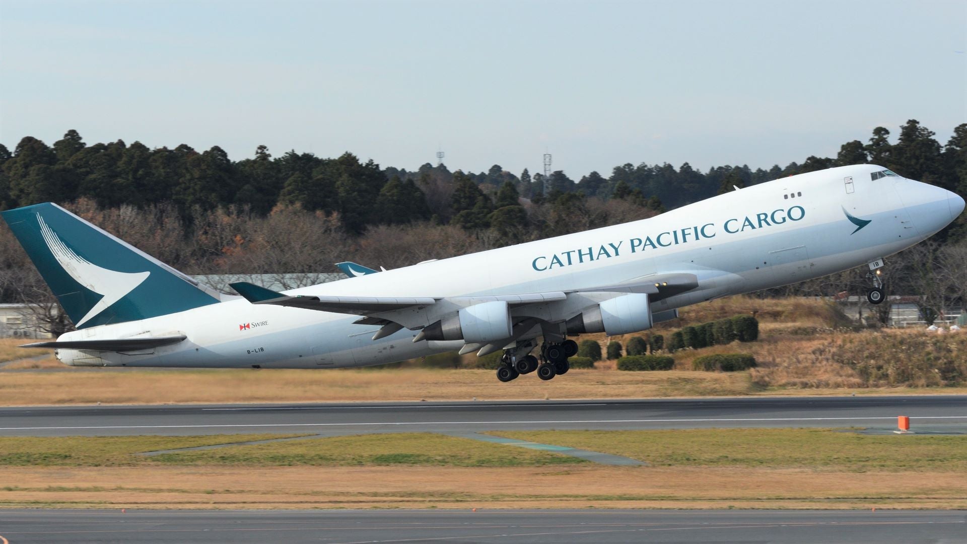 A white jumbo jet with teal tail and Cathay Pacific Cargo logo lifts off runway.