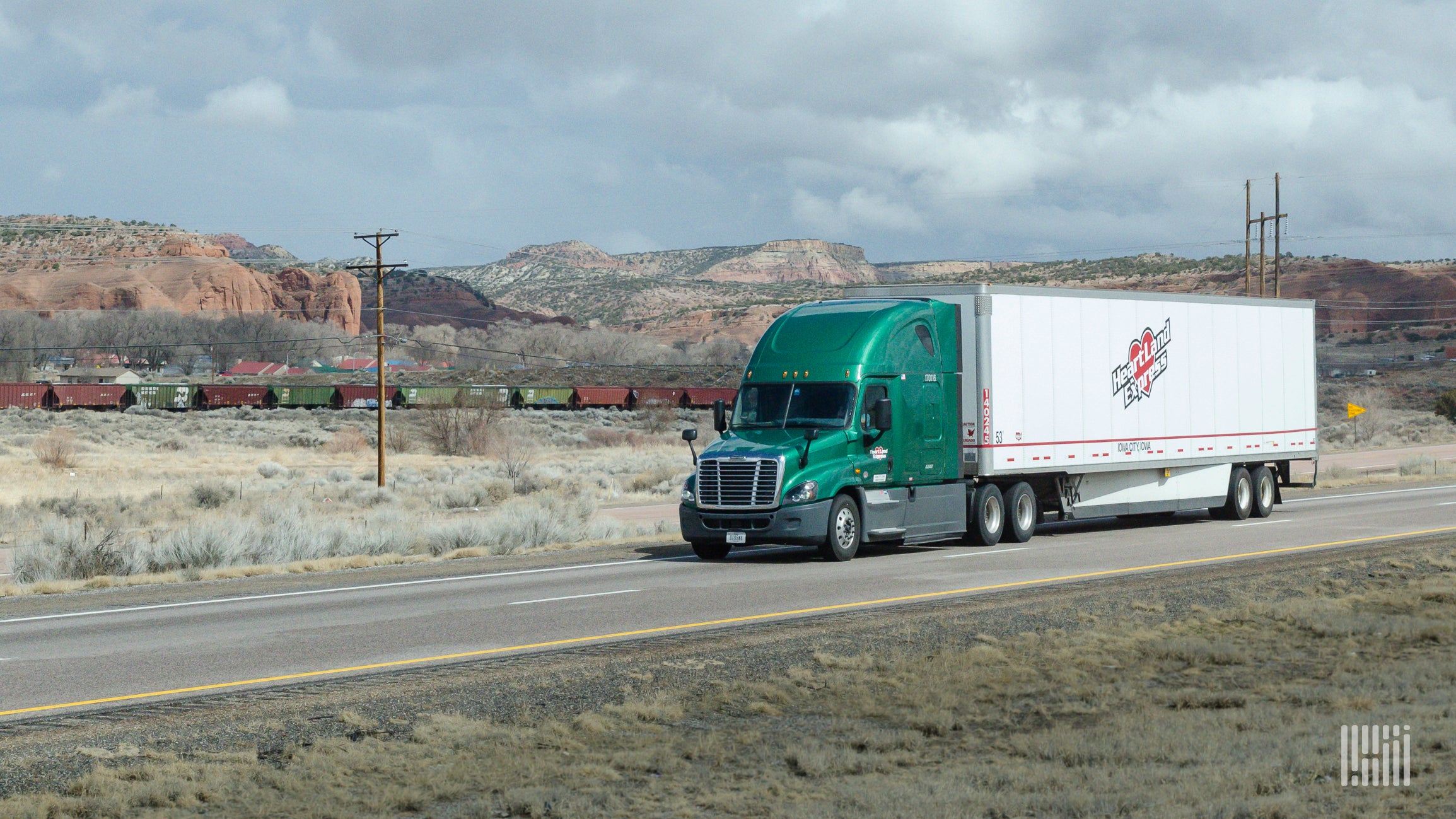 A green tractor pulling a white Heartland trailer