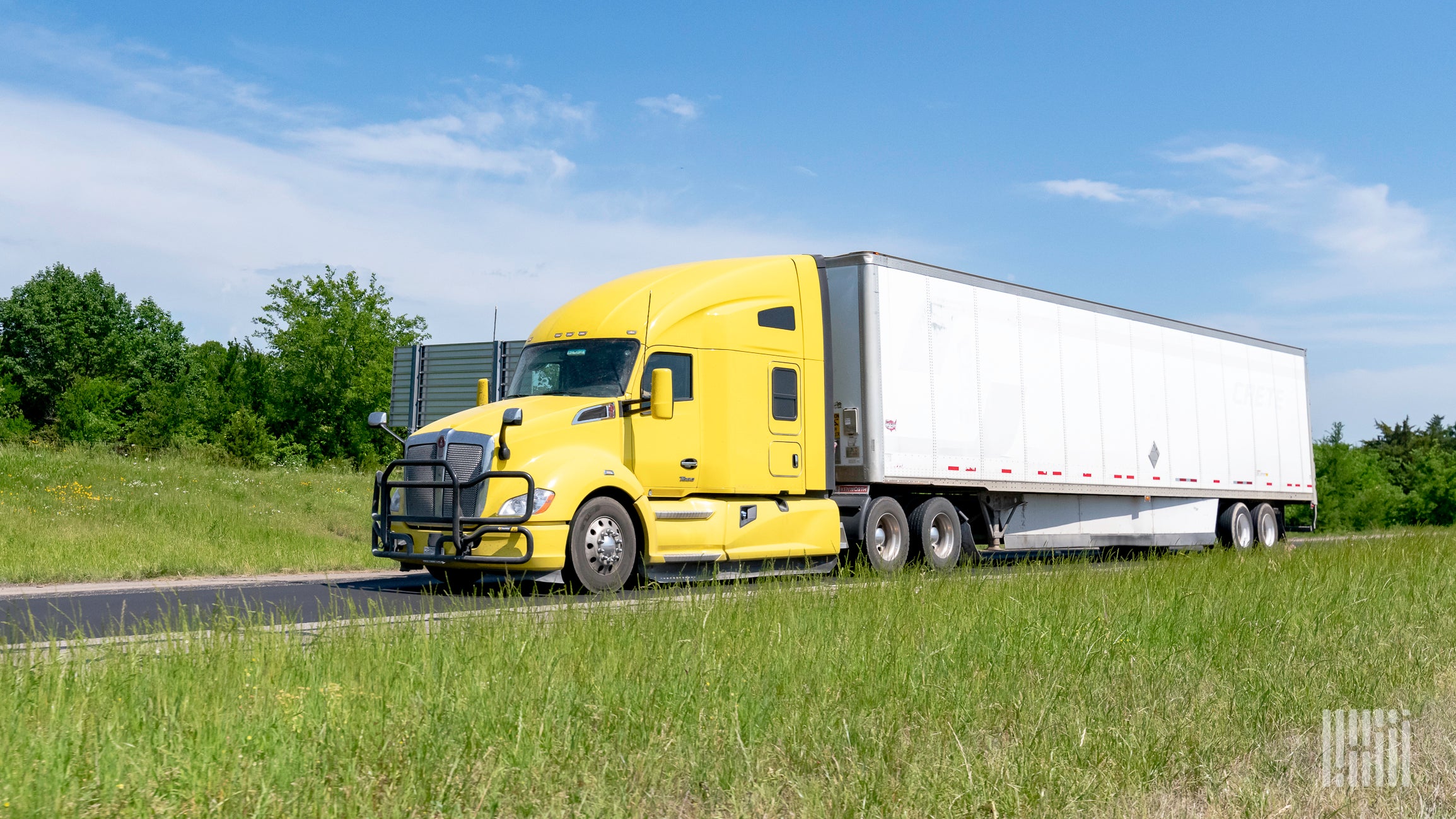 A yellow tractor pulling a white trailer on highway