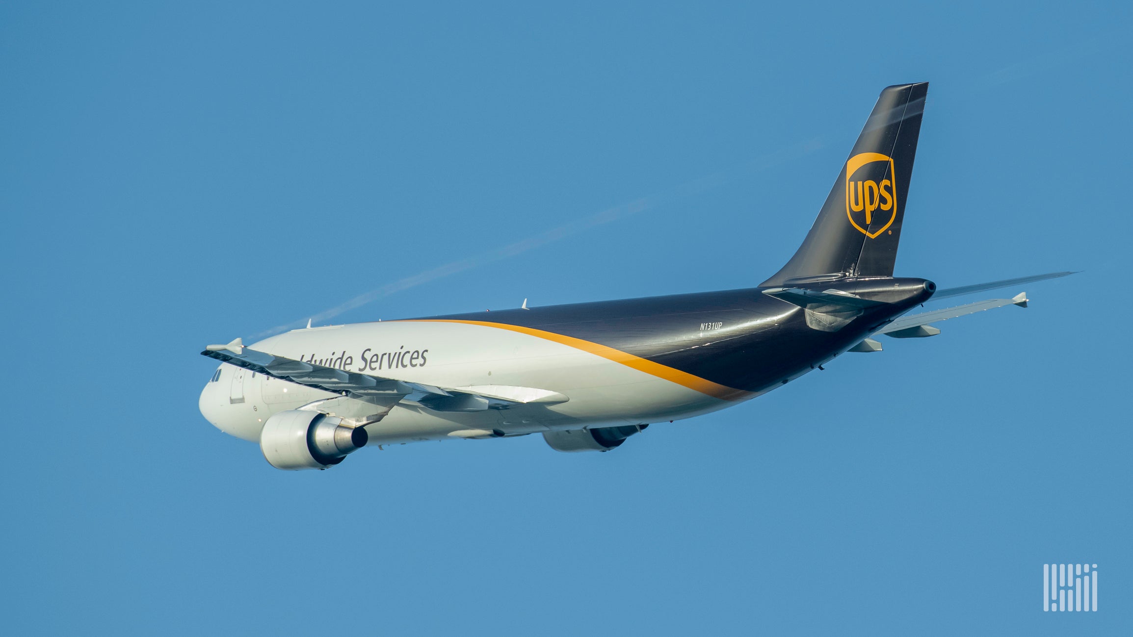 A UPS cargo plane, white in front and brown in rear, flying against blue sky, viewed from behind.