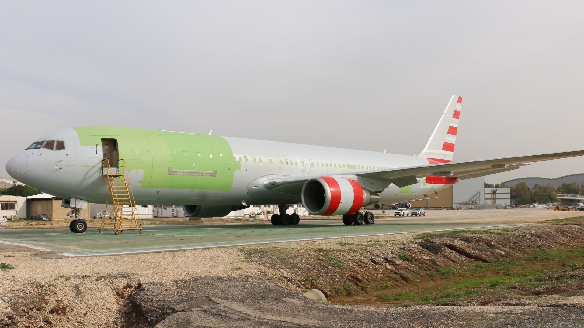 A large aircraft with paint removed and a new fuselage section as it undergoes conversion for freight service.