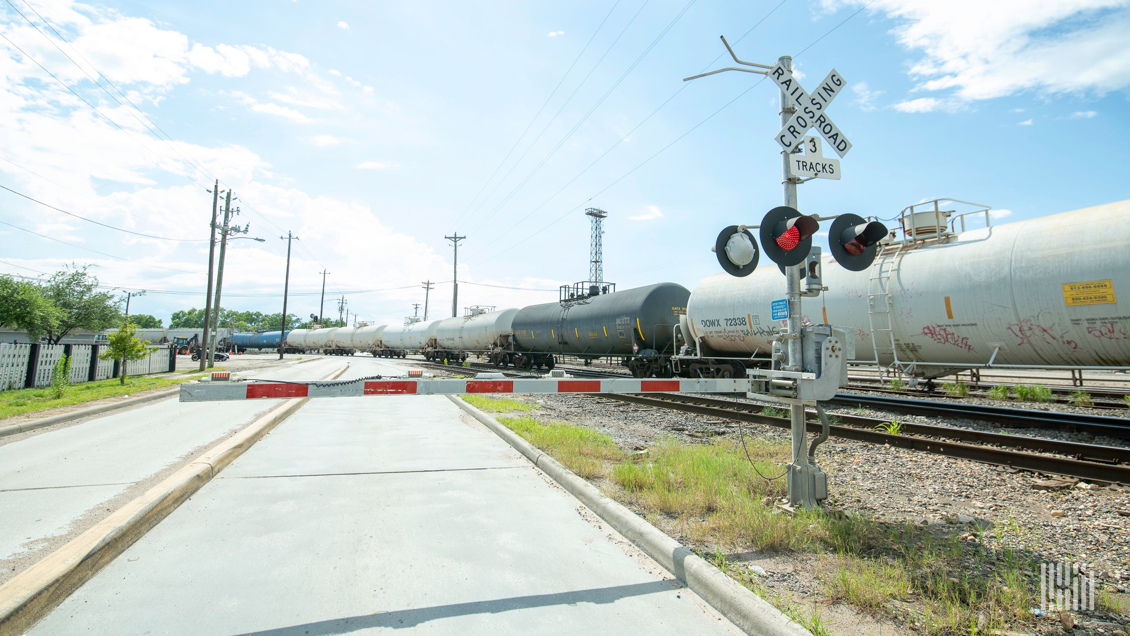 A train of tank cars passes by a railroad crossing