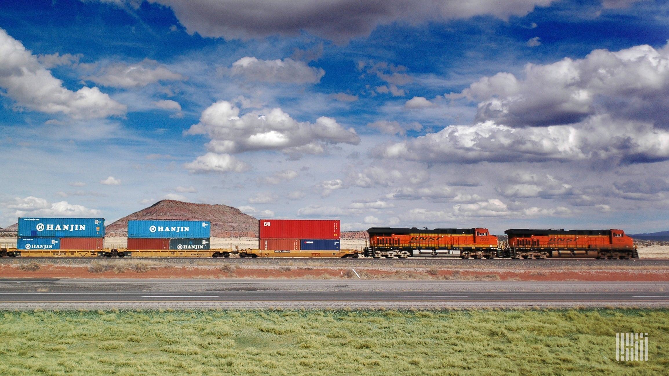 A BNSF locomotive hauls intermodal containers across a grassy field.