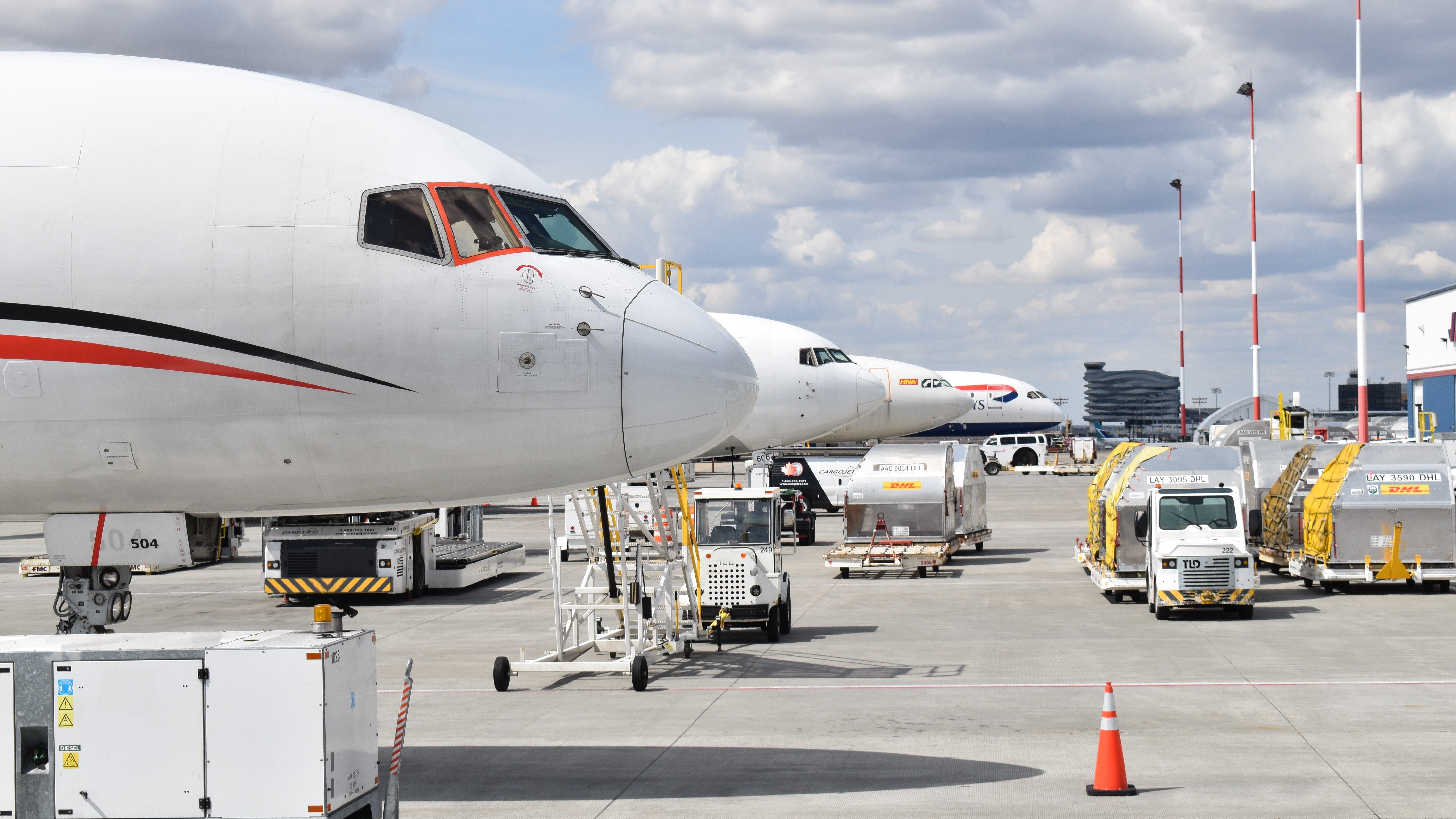 Side nose view of large, white commercial jets in a row at airport on sunny day.