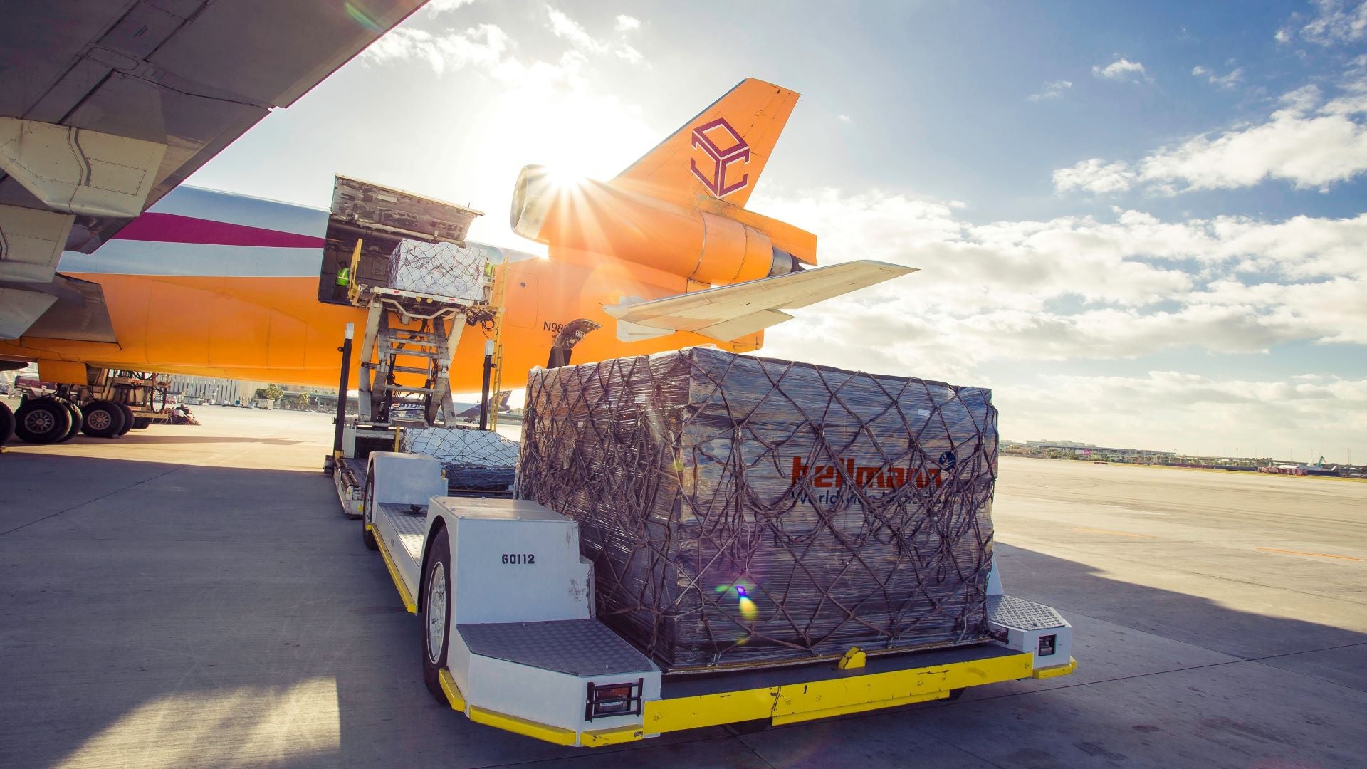 A pallet of cargo on a flat pad waiting to be loaded on a yellow airliner.