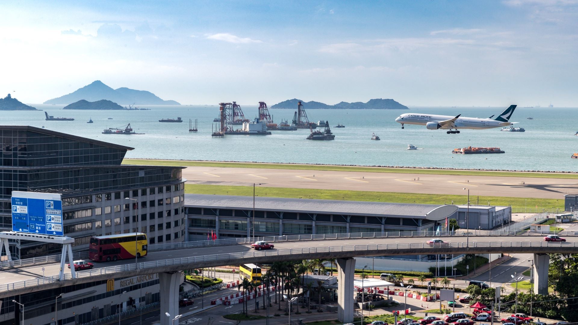 A plane comes in for a landing in Hong Kong with ocean view beyond runway.