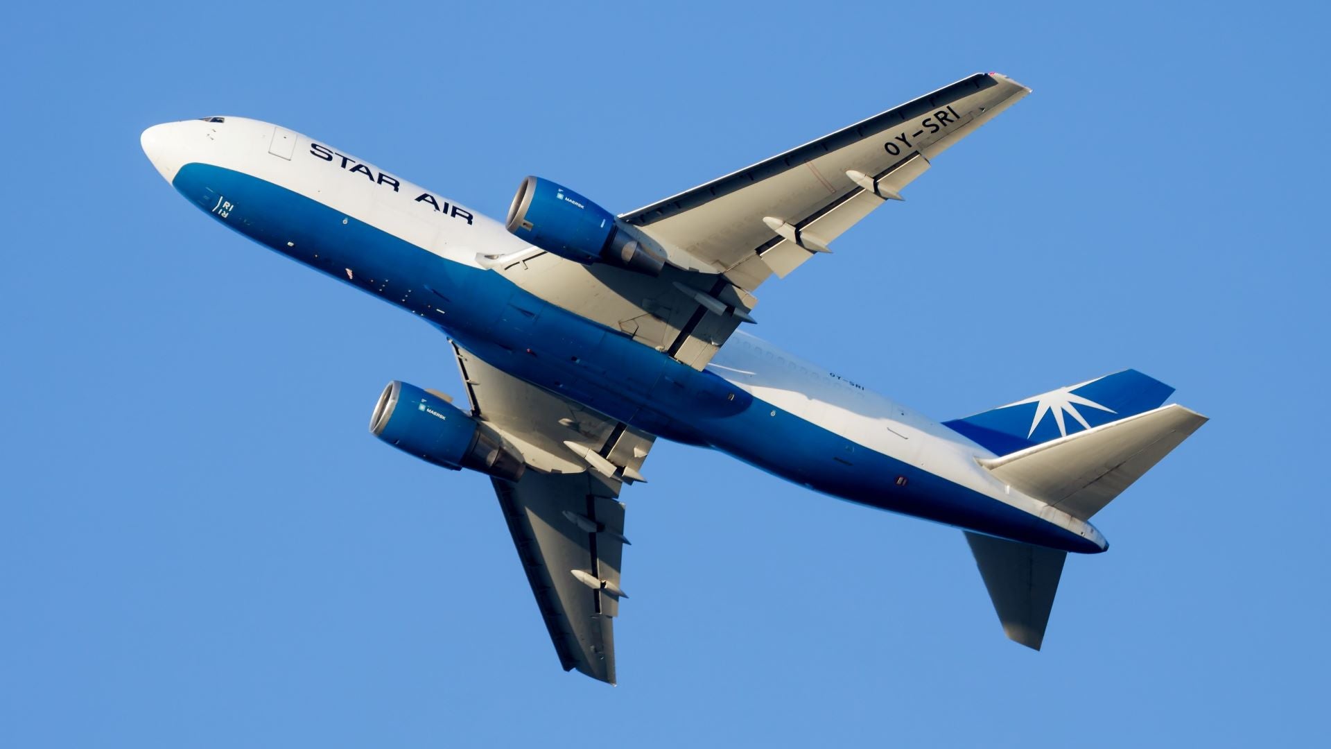 A white-blue Star Air jet as seen from below against blue sky.