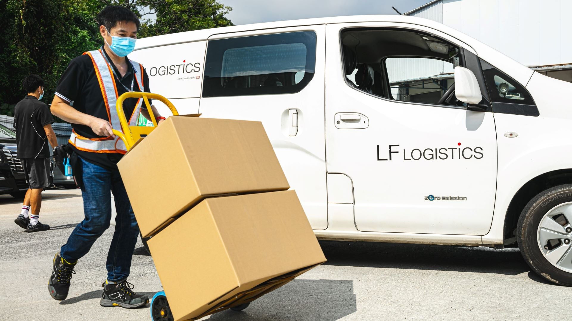 A worker moves boxes on a handcart after unloading from a white LF Logistics van.