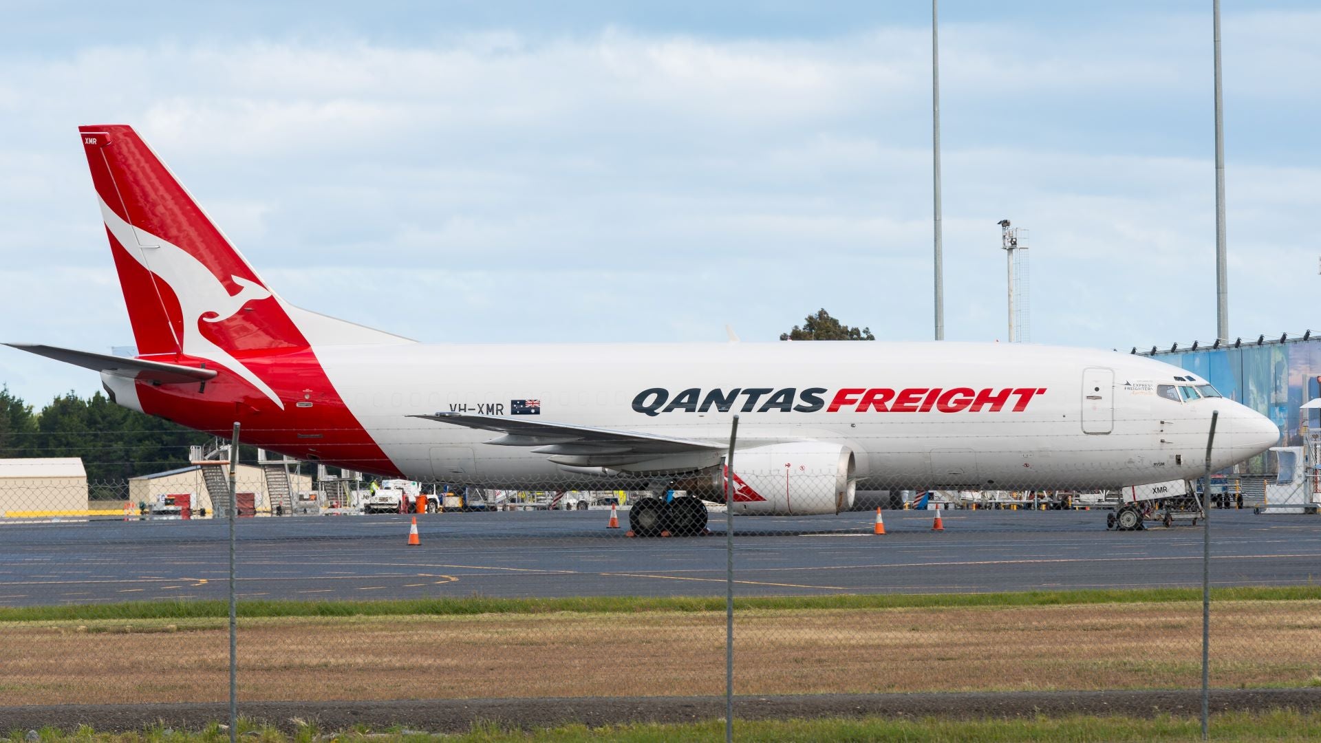 A white with a red tail and Qantas kangaroo logo sitting an an airport apron.