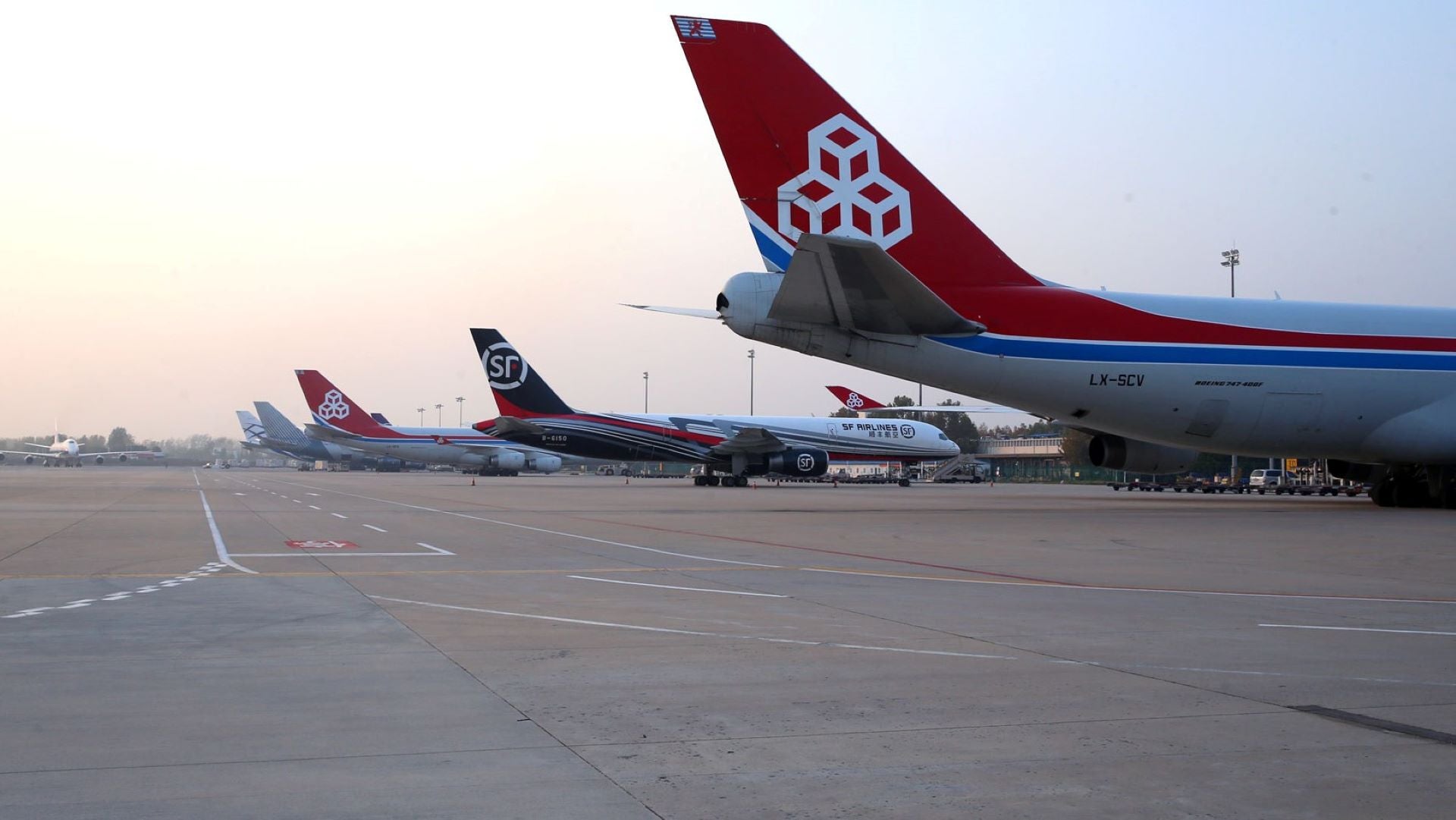 Tail sections of cargo jets lined at an airport terminal in early morning.