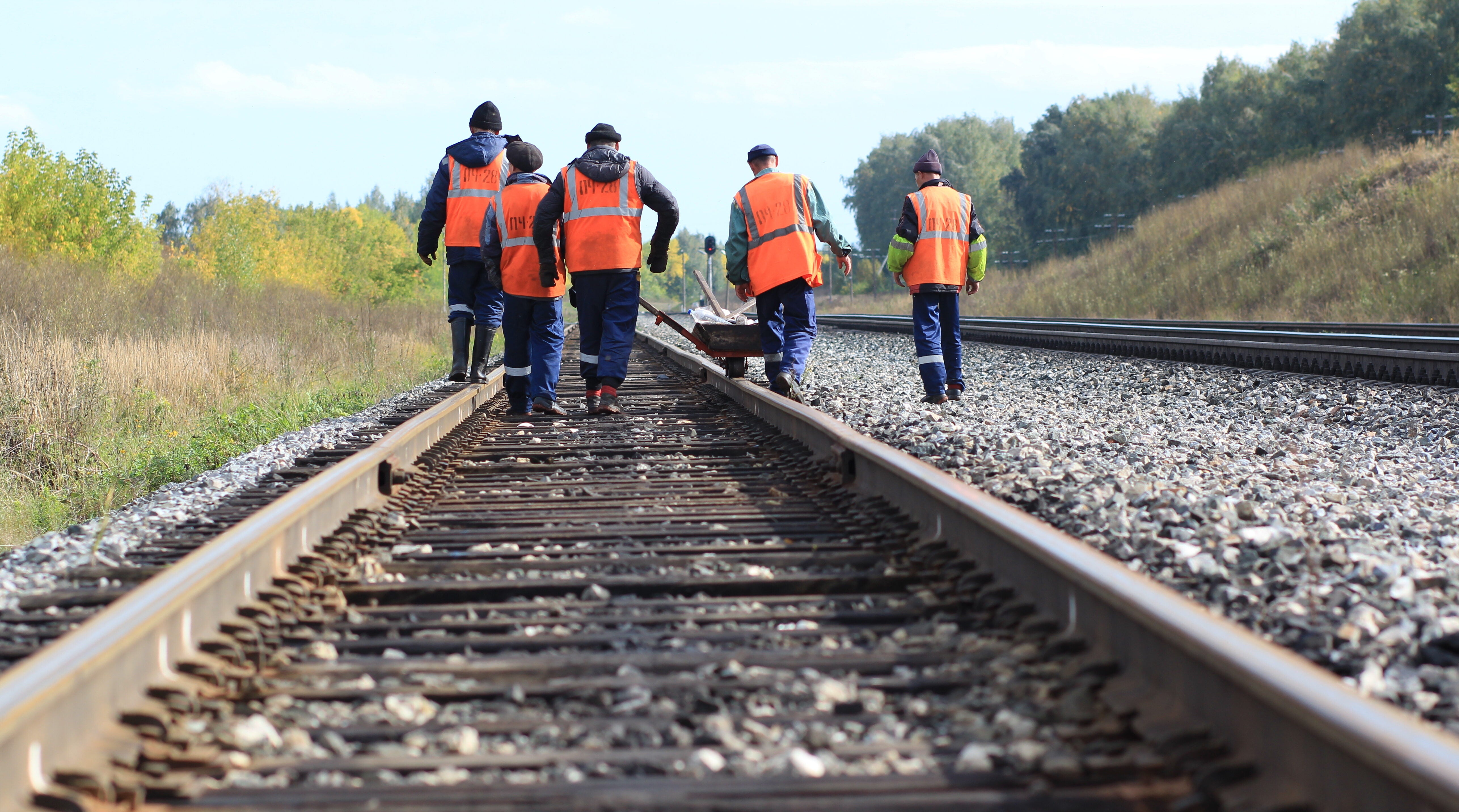 A group of five people walking on railroad tracks and wearing orange work vests.