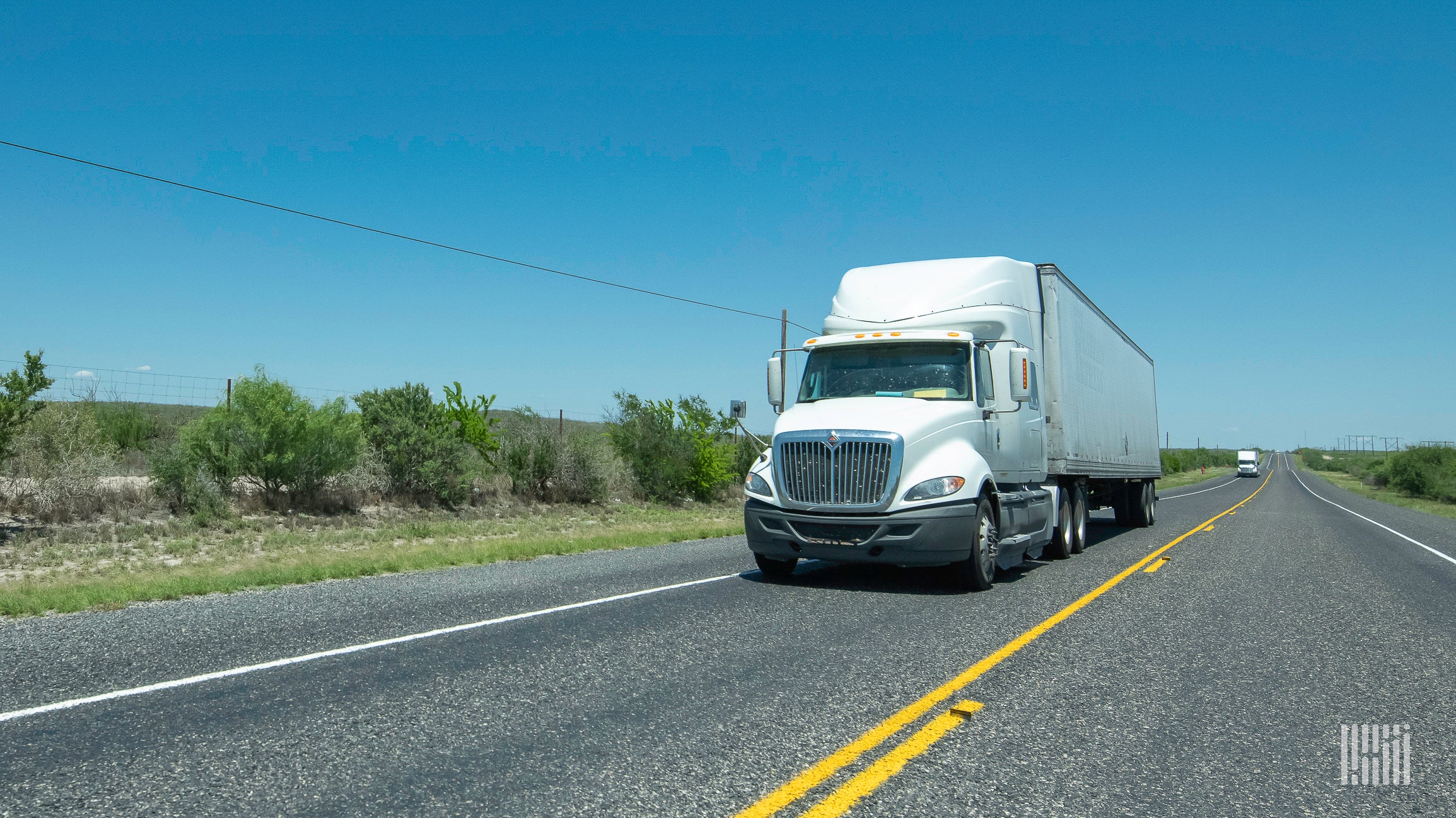 A white tractor pulling a trailer on the highway