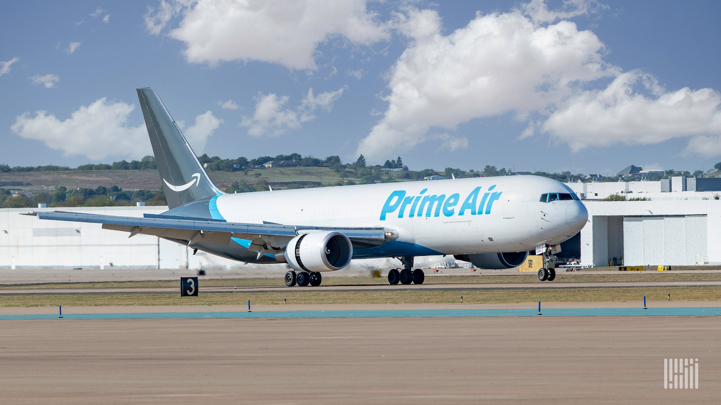 A white Amazon Prime jet with blue accents landing at an airport.