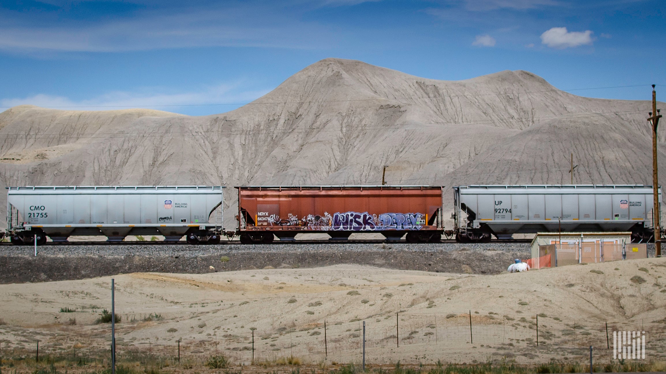 A train hauling hopper cars passes through a desert.