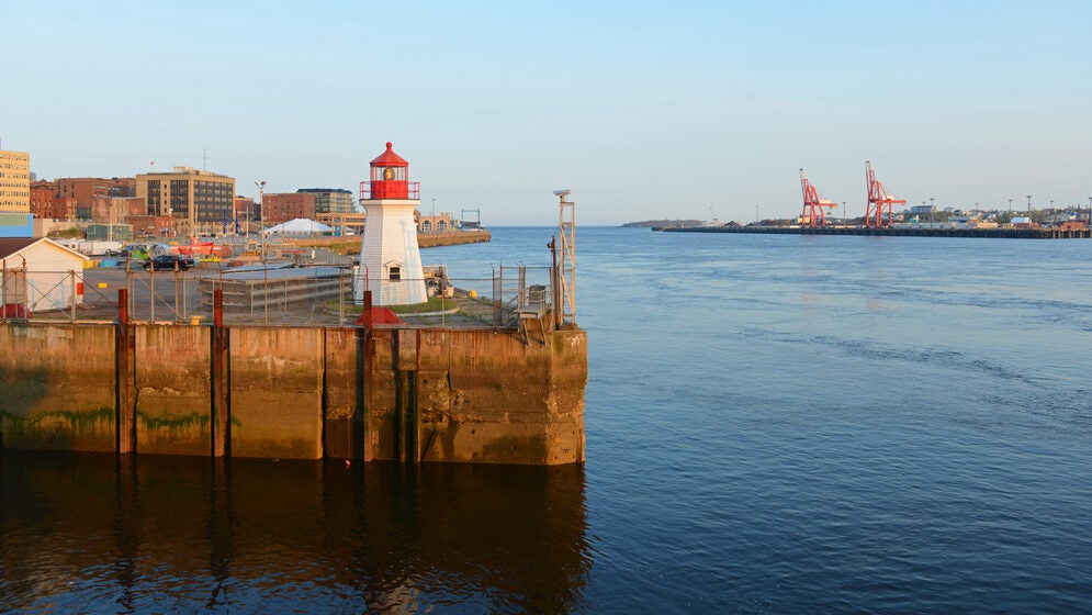 A lighthouse at a pier's edge stands watch over a harbor.